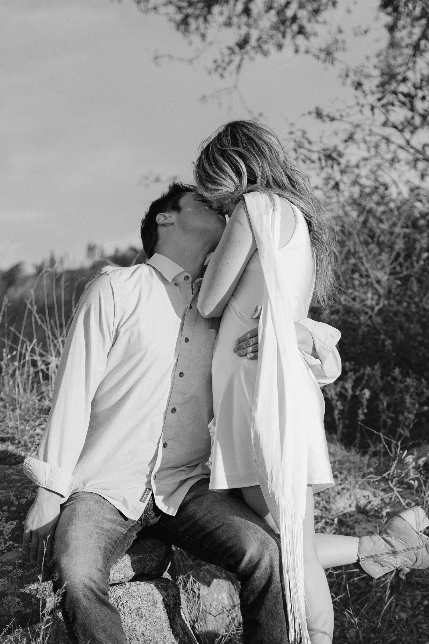 Black and white photo series showing a romantic couple in white clothing embracing outdoors in a natural setting.
