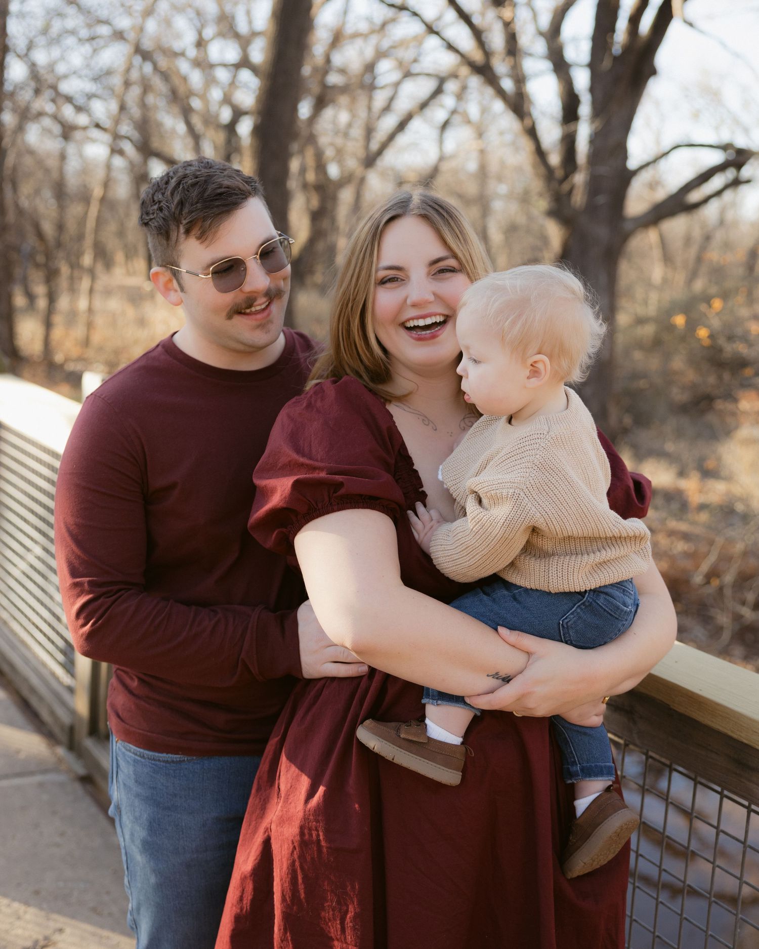 Loving family moment captured by a lake with warm burgundy and beige color coordination.