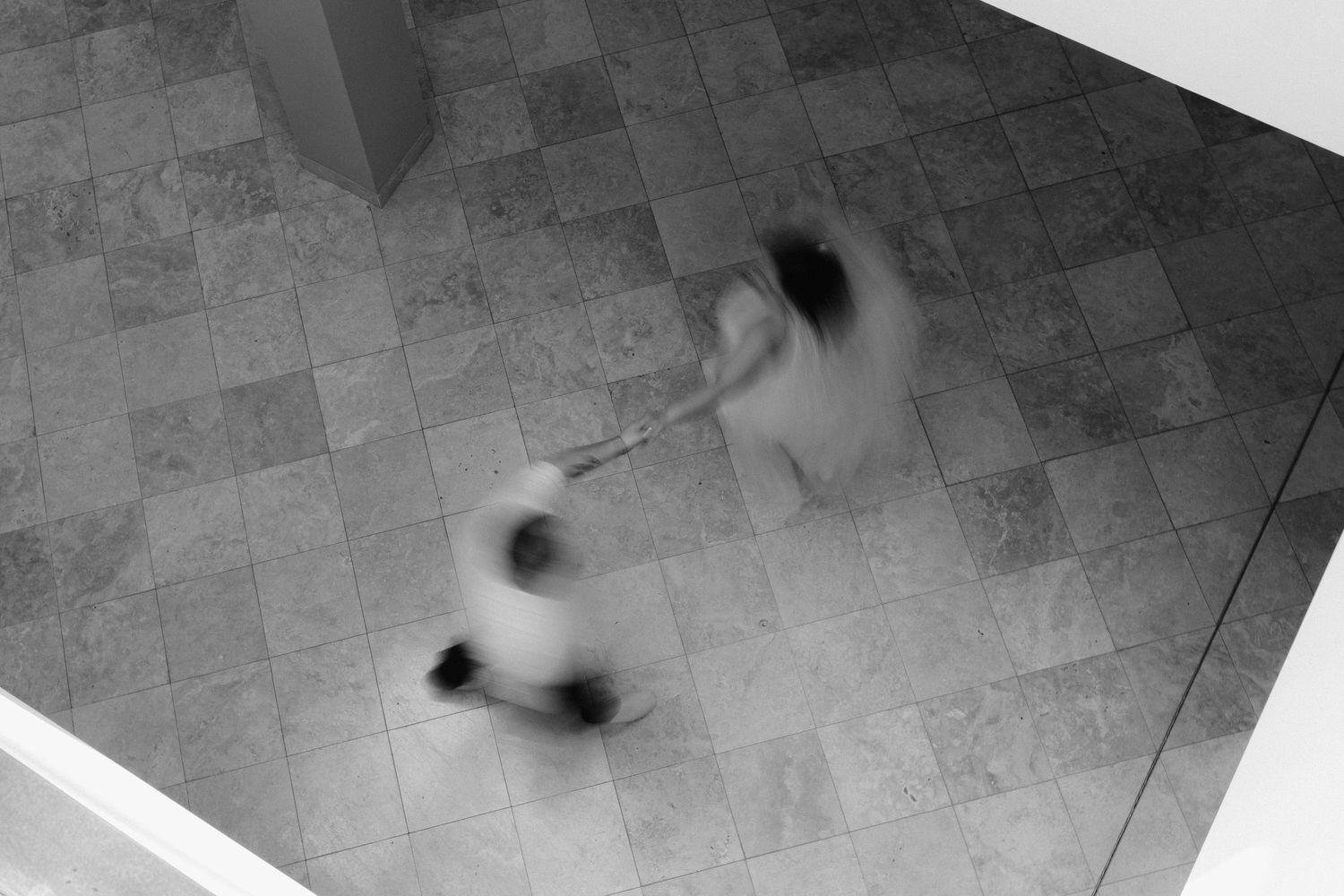 Blurred black and white overhead shot of two figures in motion on a tiled floor.