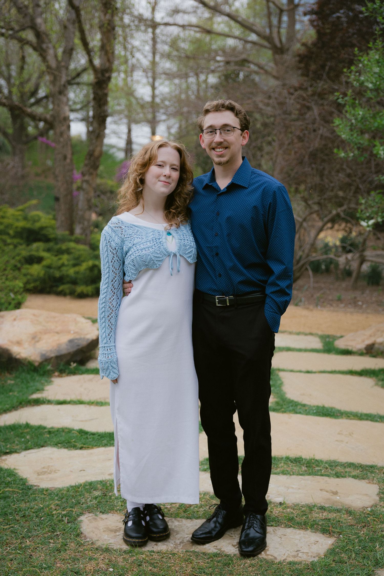 Couple in coordinated blue and white outfits pose together on stone pathway outdoors.