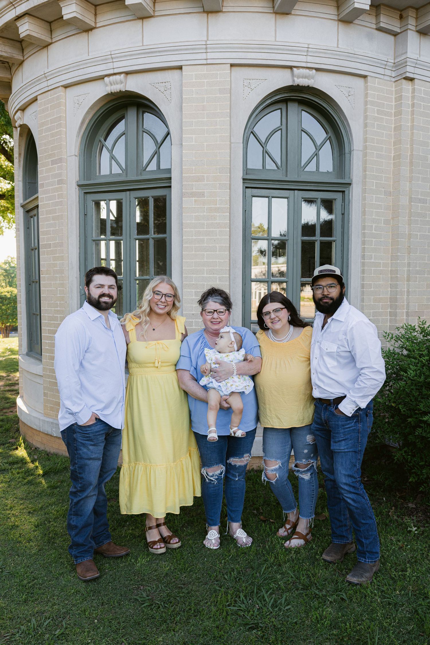 A group poses in front of an elegant stone building with arched windows on a sunny day.