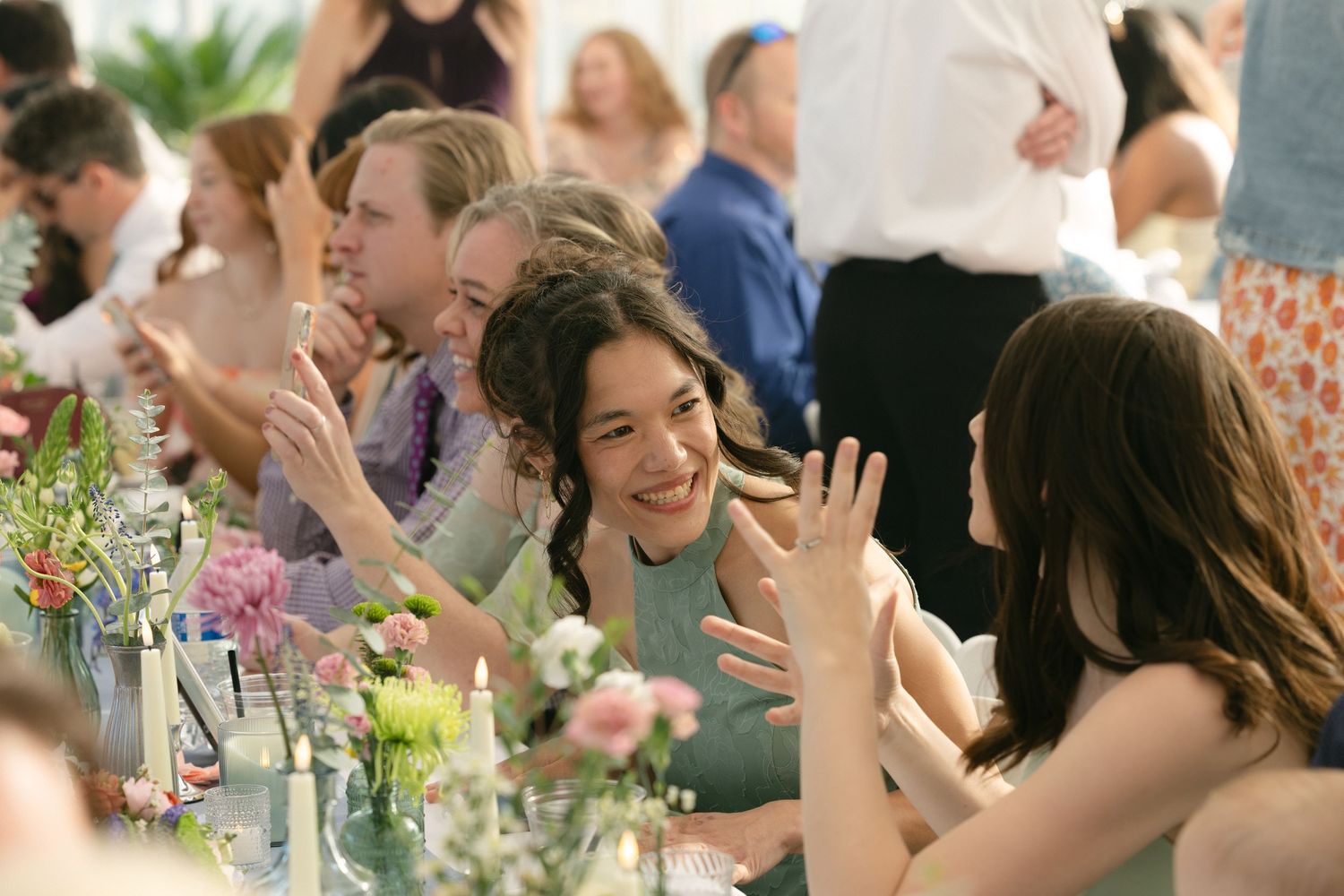 Guests laughing and clapping at a wedding reception table adorned with candles and pink floral arrangements.