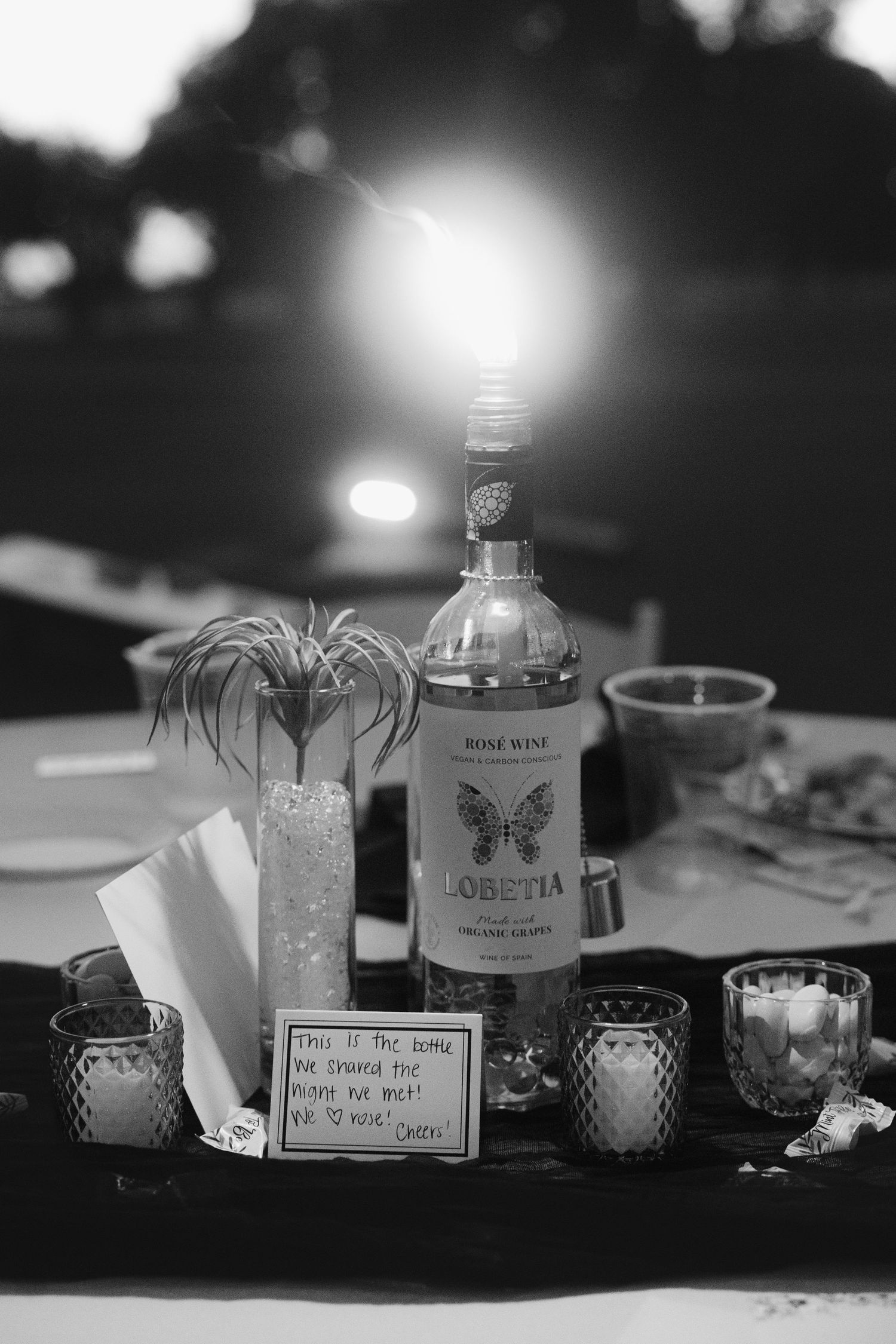 Black and white wedding table centerpiece with rose wine bottle, candles, and a heartfelt note.