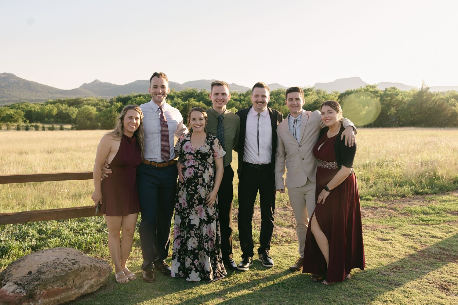 Group of wedding guests posing together in front of scenic mountain landscape at sunset.