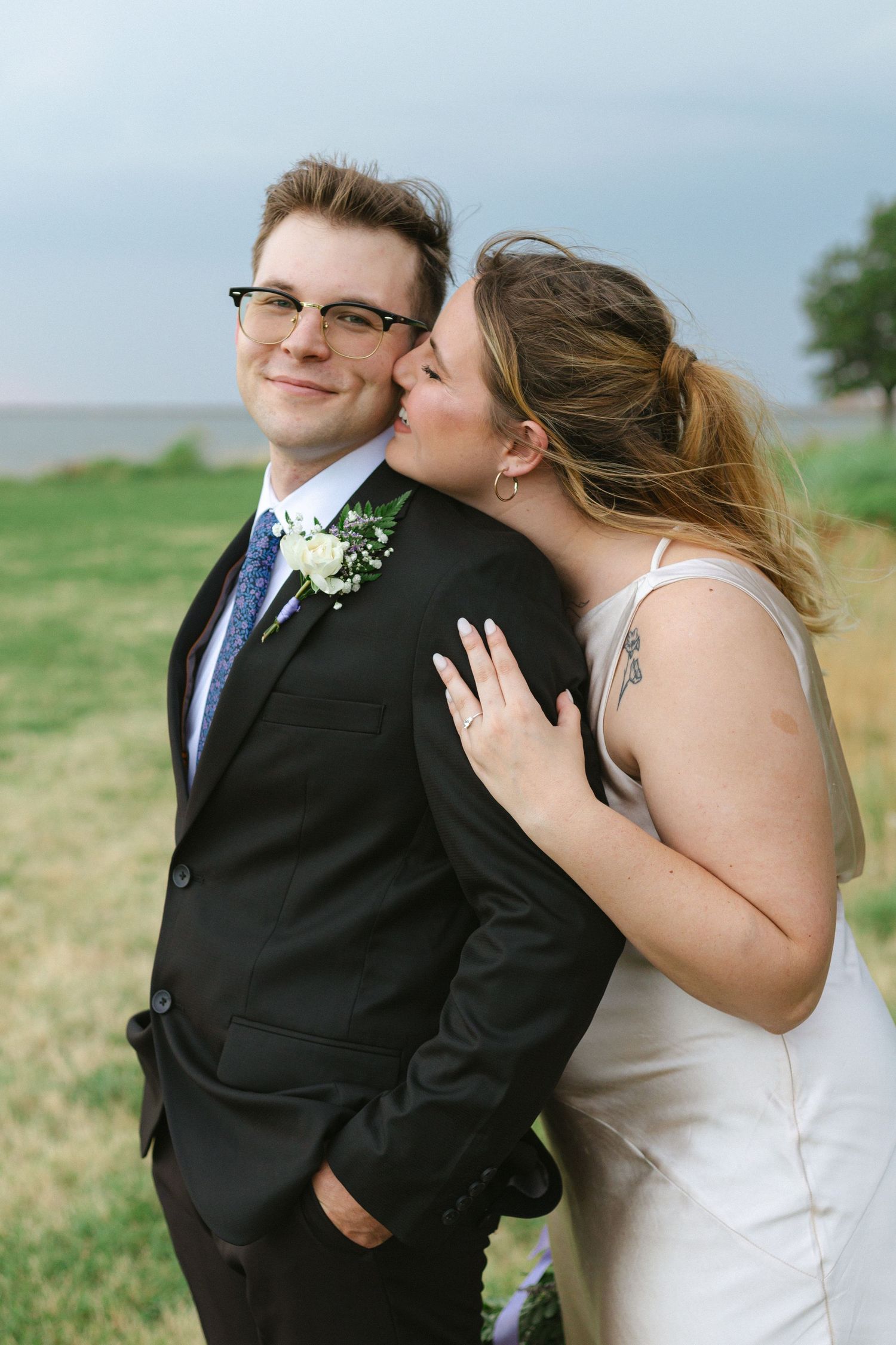 A romantic outdoor wedding photo series showing a bride playfully kissing the groom in an open field.