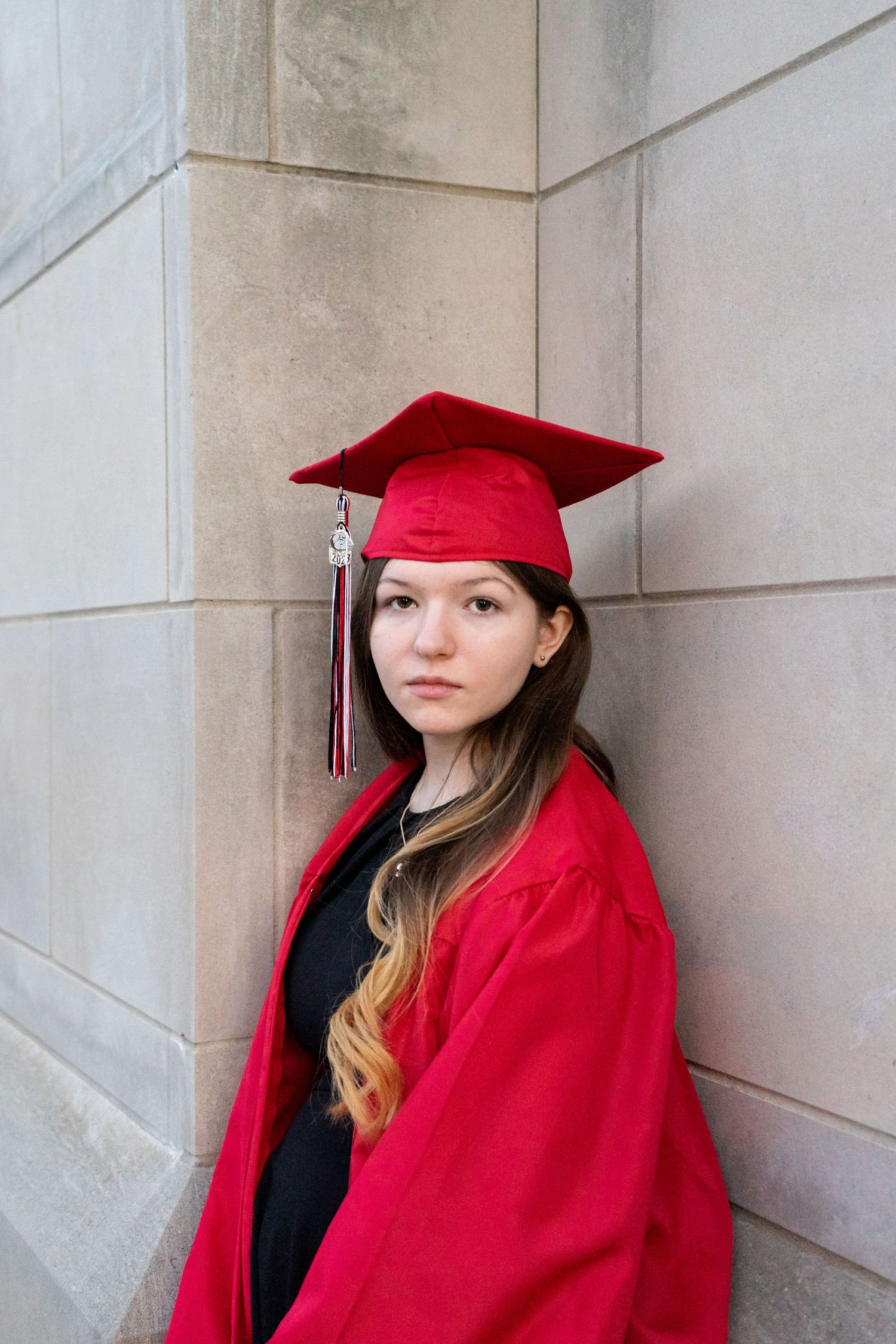 Graduate in red cap and gown standing against stone wall in series of portraits.