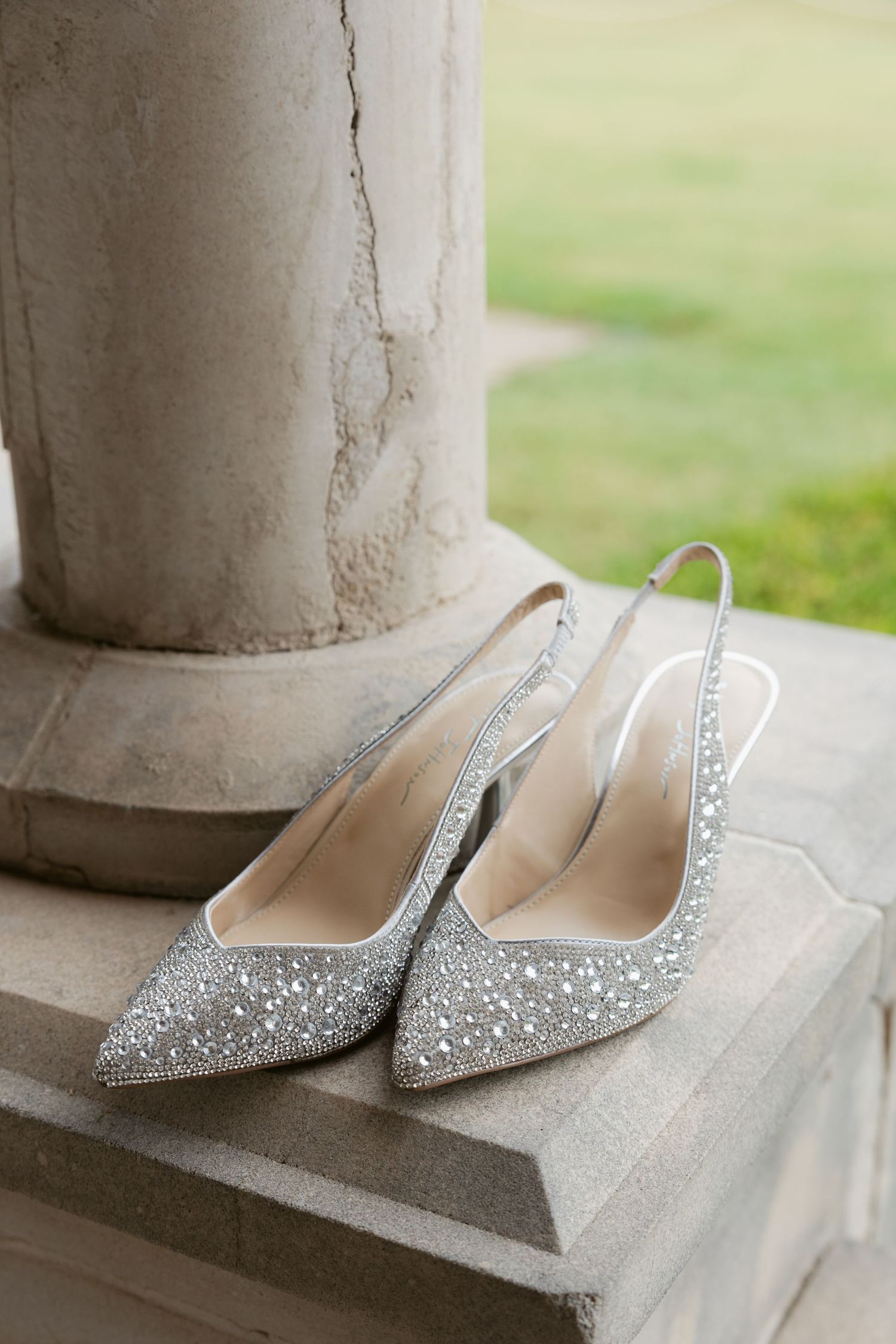 Elegant silver glitter bridal shoes with pointed toes displayed on a stone ledge in natural lighting.