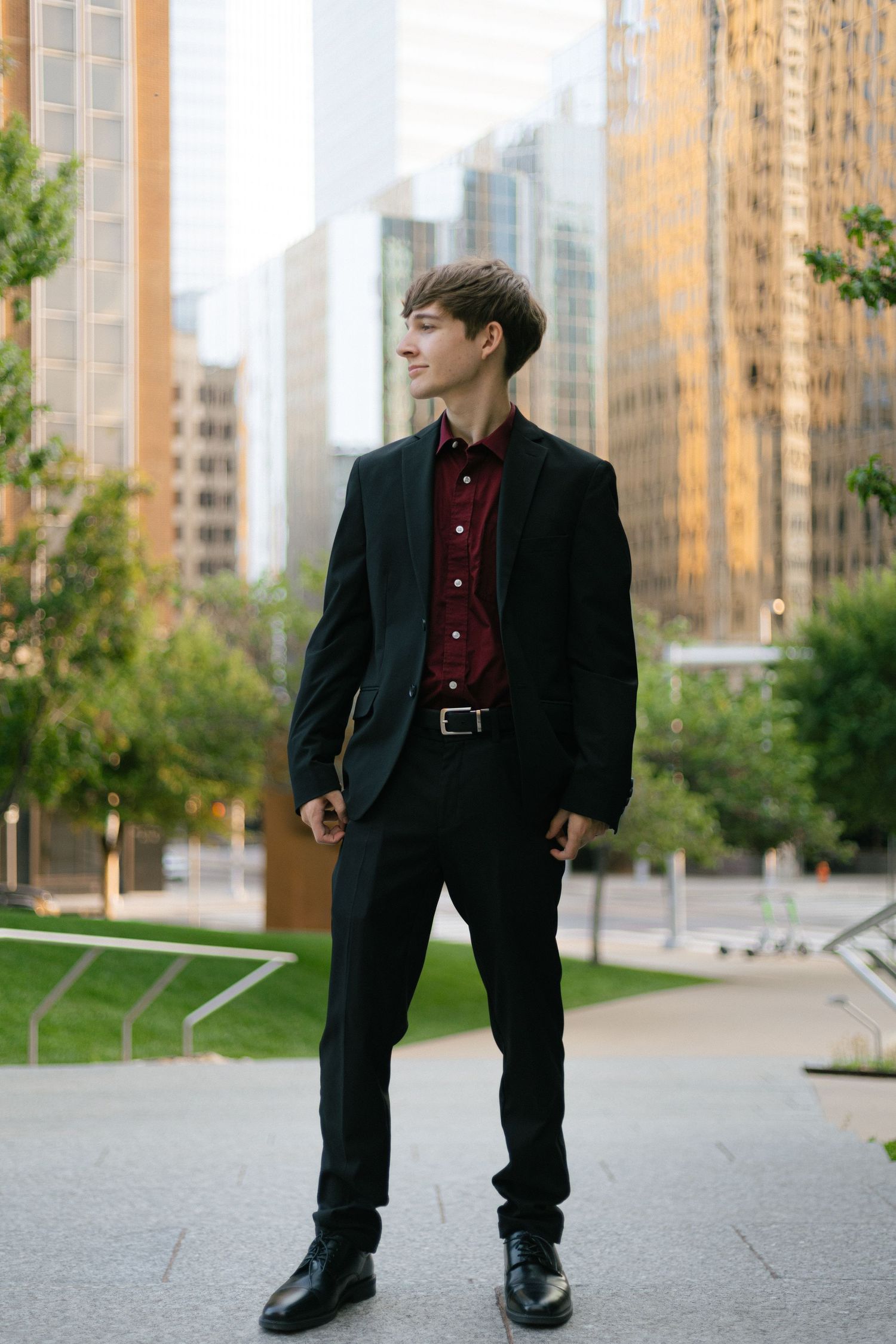 Stylish person in dark suit poses against urban cityscape with tall buildings.