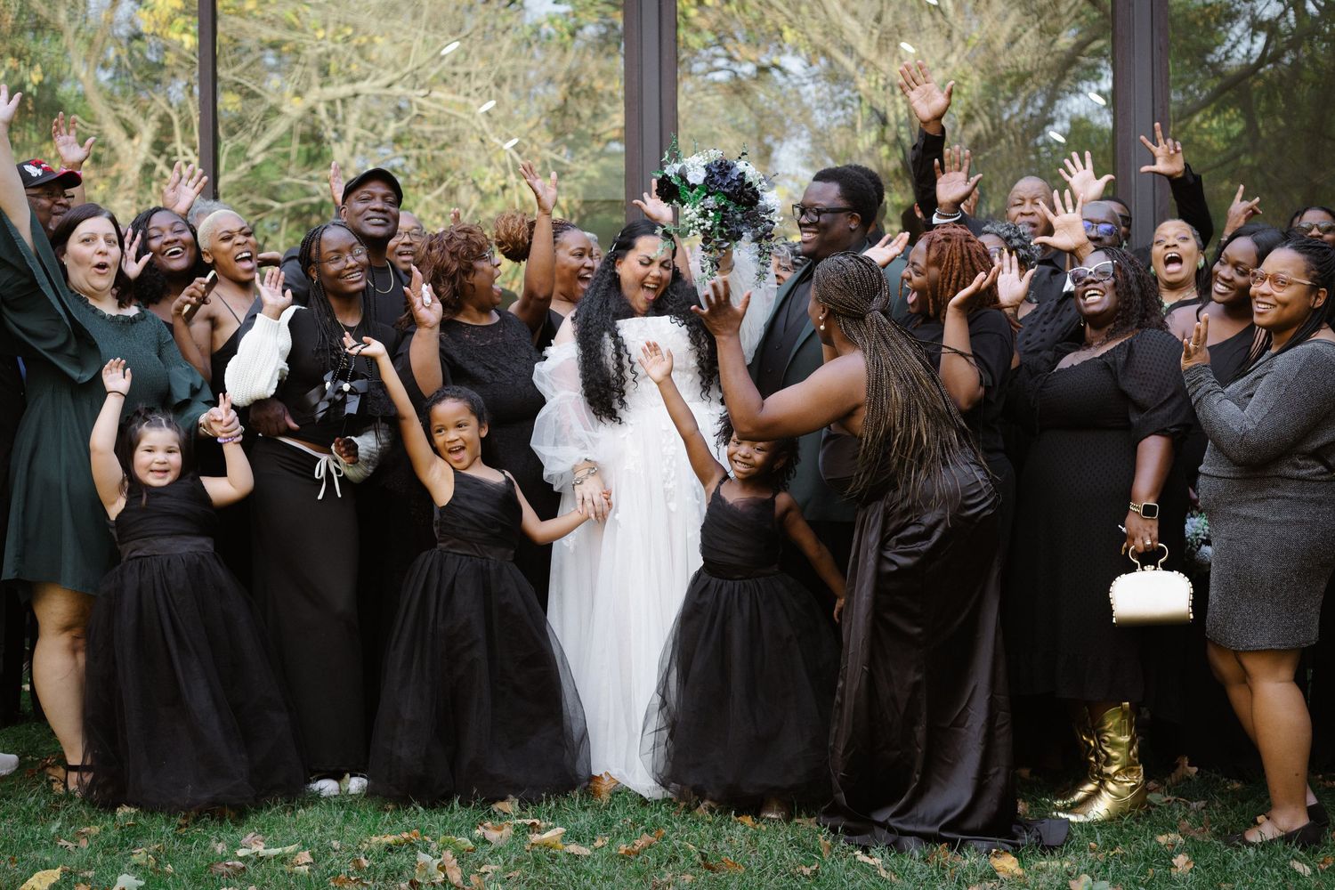Wedding party in black and white attire poses joyfully together outdoors during celebration.