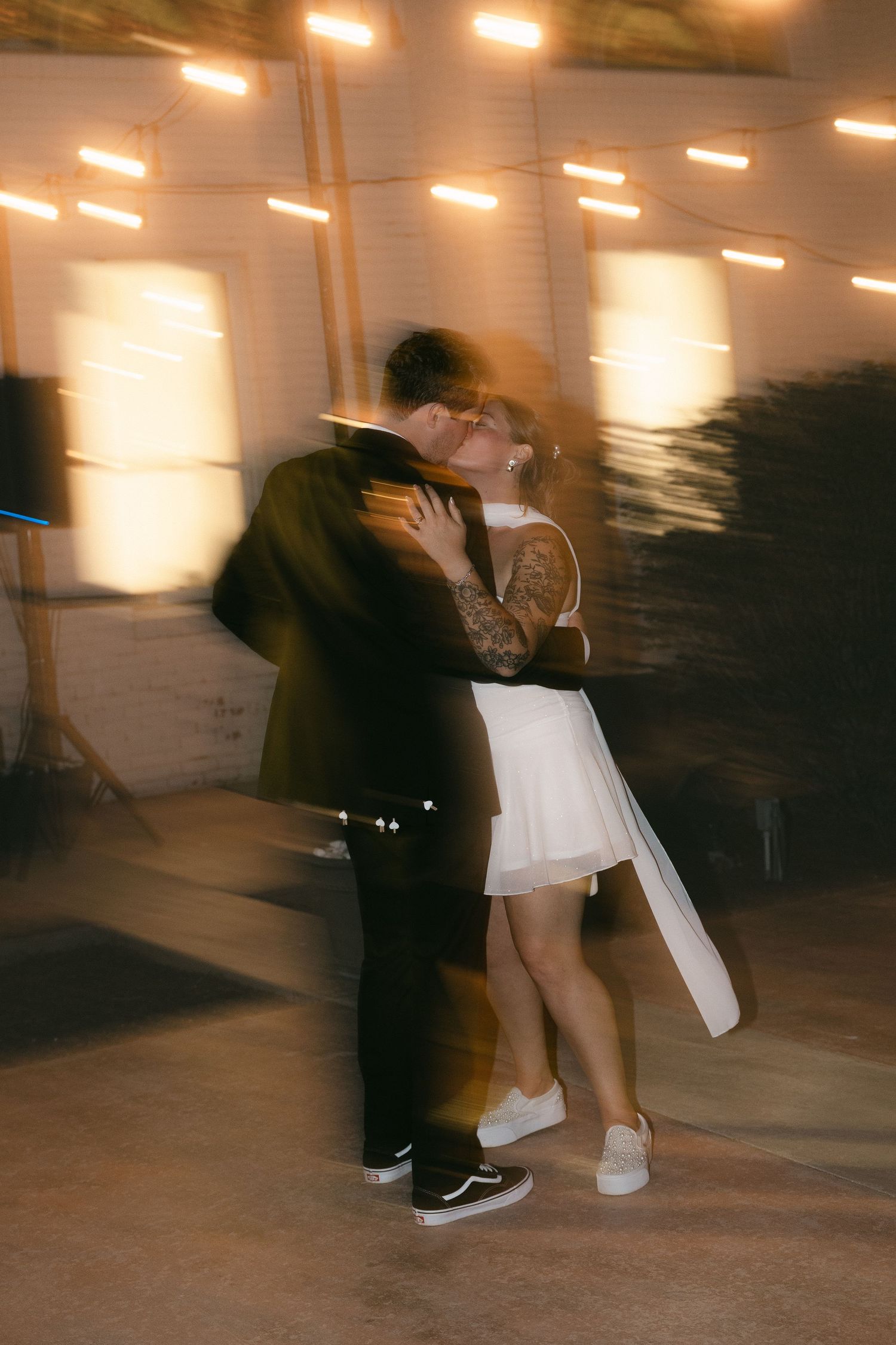 Couple sharing a romantic first dance kiss at their wedding reception, bride in white mini dress and groom in dark suit.