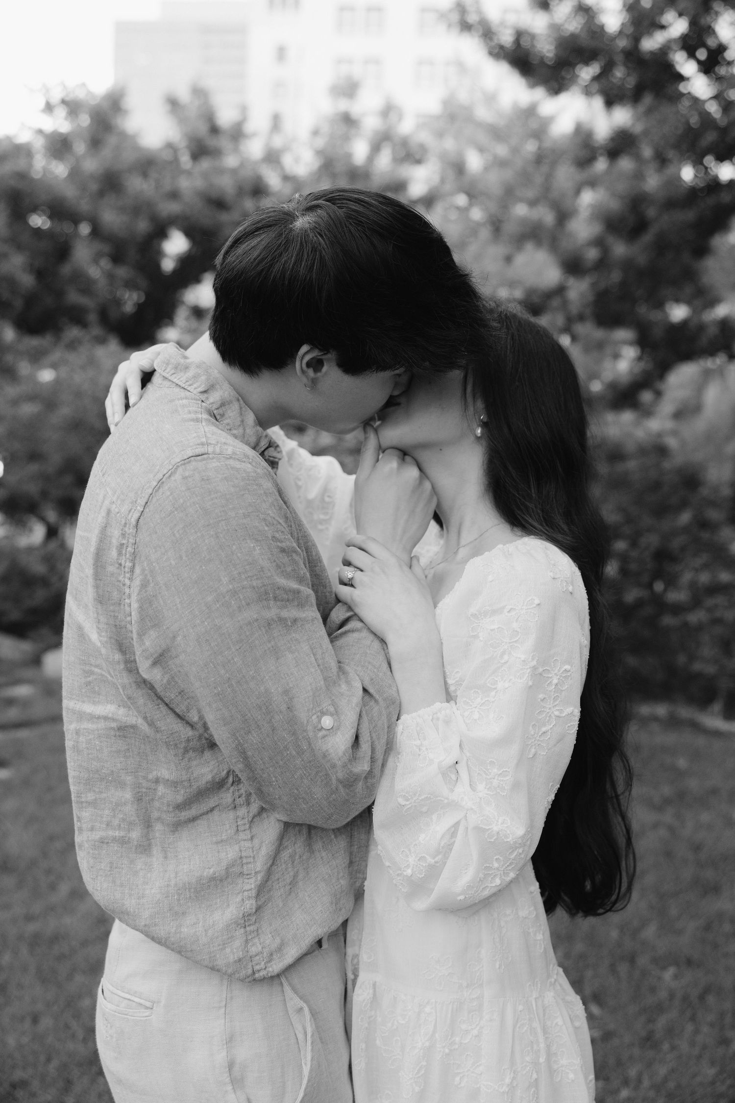 Black and white photo of a tender embrace between a couple in a garden, woman in white dress holding man close.