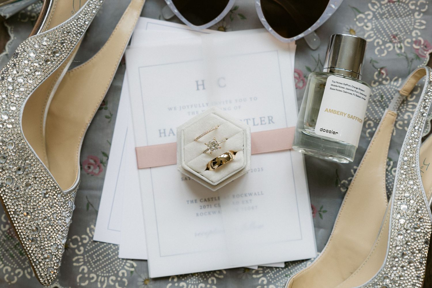 Elegant wedding details including invitations, rings, and delicate lace accessories arranged on a light gray surface.