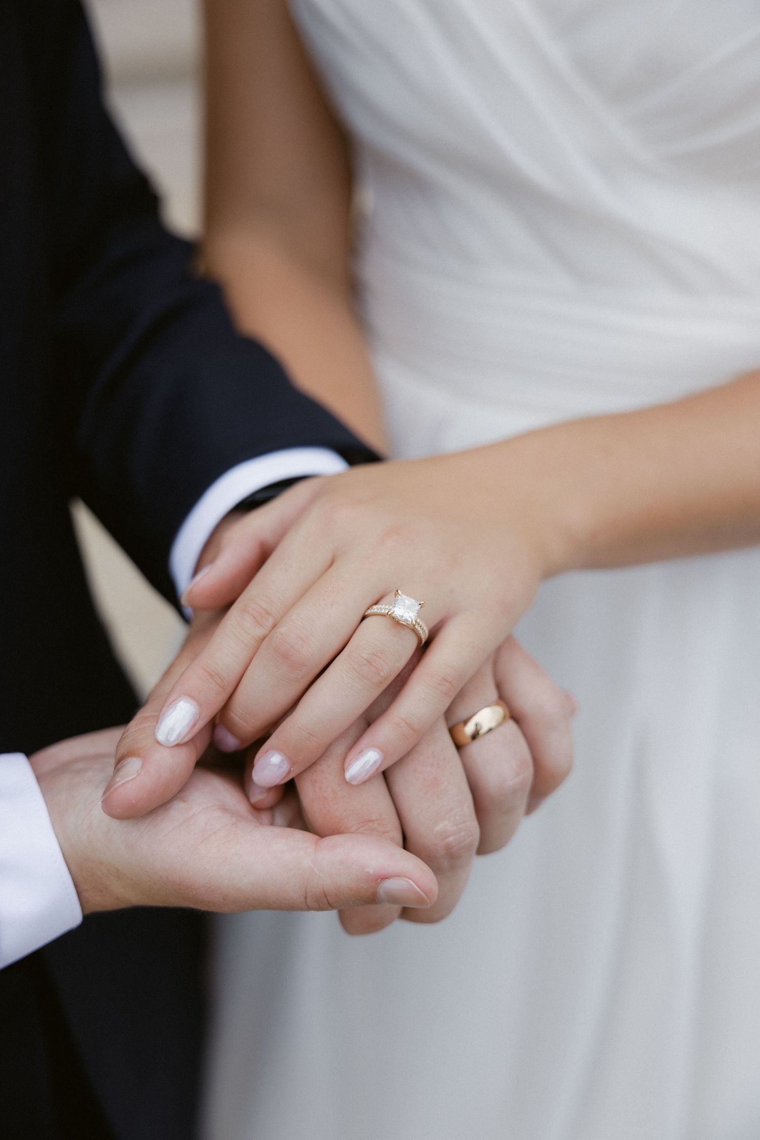 Close-up of newlywed couple's hands with wedding rings showing tender embrace.