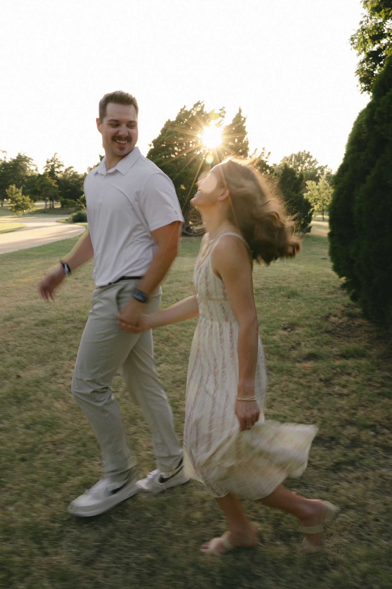 A man and young girl hold hands dancing in a sunny park at golden hour, her dress spinning with joy.