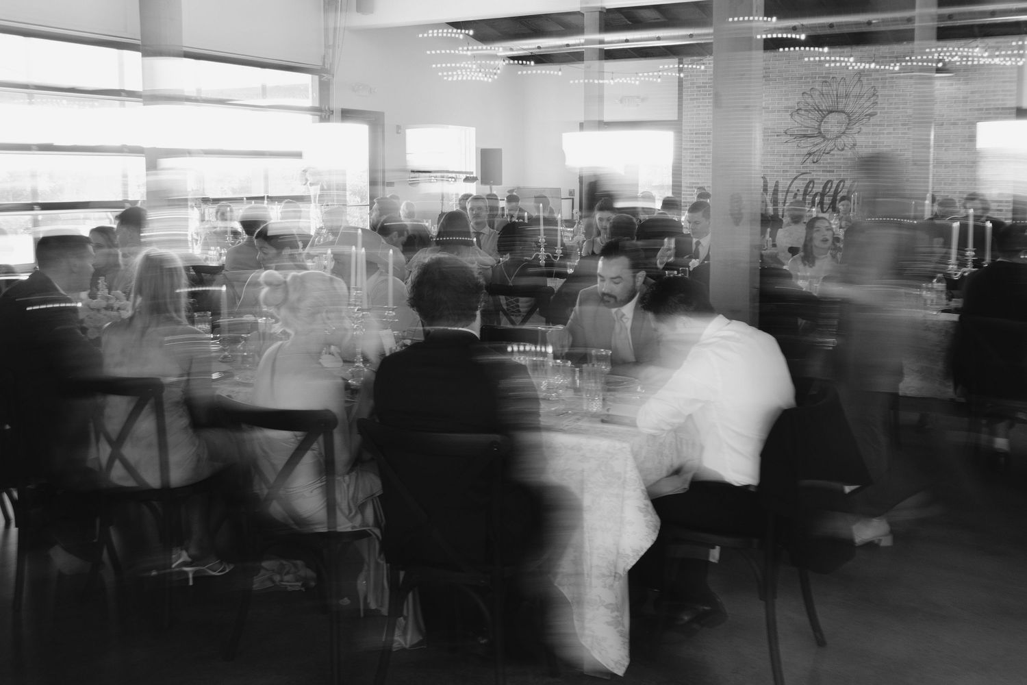 Blurred black and white photo of guests seated at tables during a wedding reception.