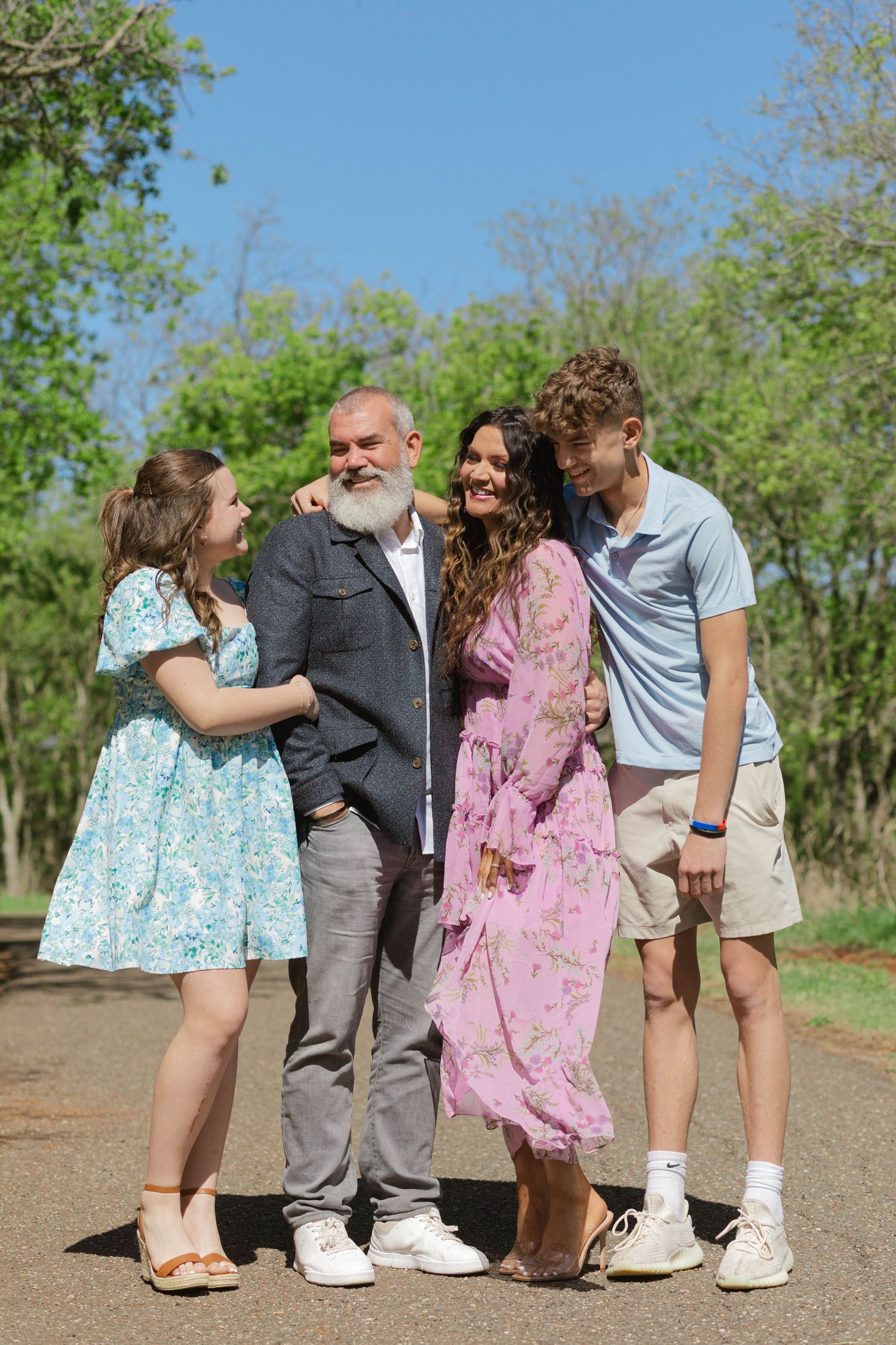 Family group standing together on a path surrounded by green trees on a sunny day.