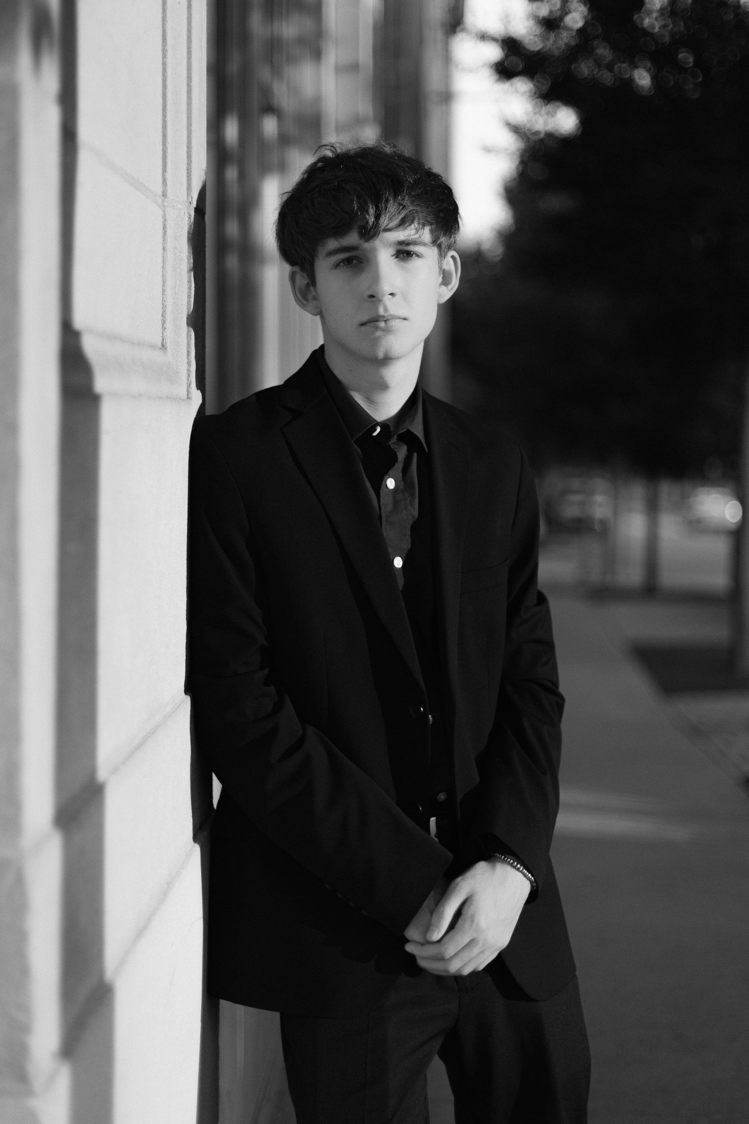Classic black and white portrait of person in formal attire against building wall.