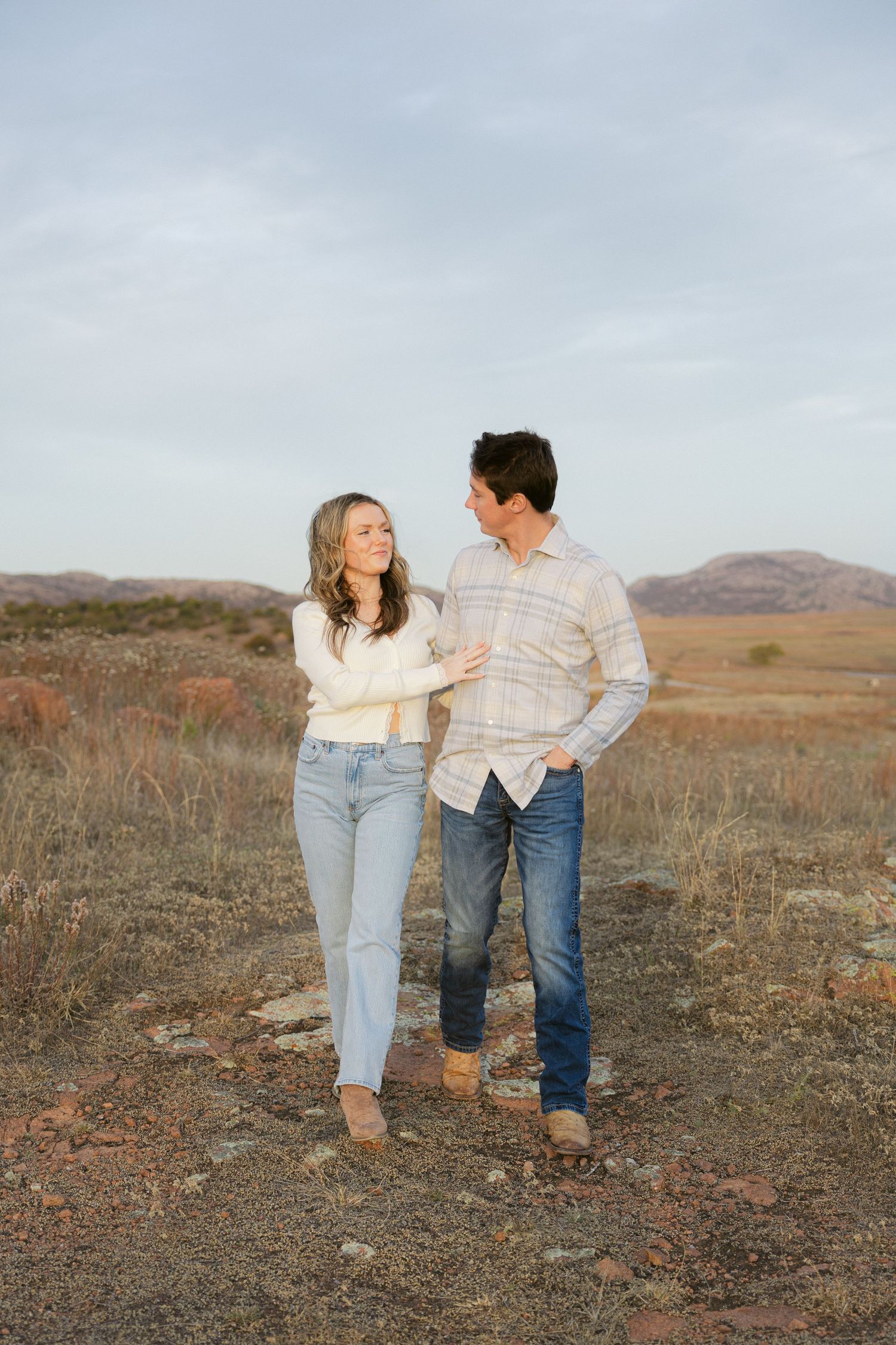 A couple walks together through a scenic desert landscape at sunset, holding hands and sharing joyful moments.