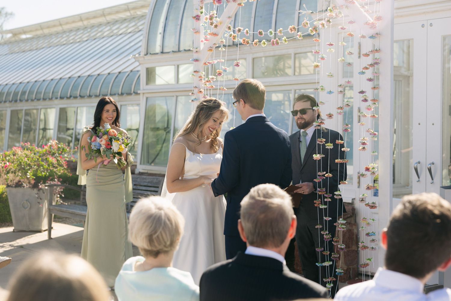 Bride and groom exchange vows outdoors at a botanical garden wedding ceremony with guests seated.
