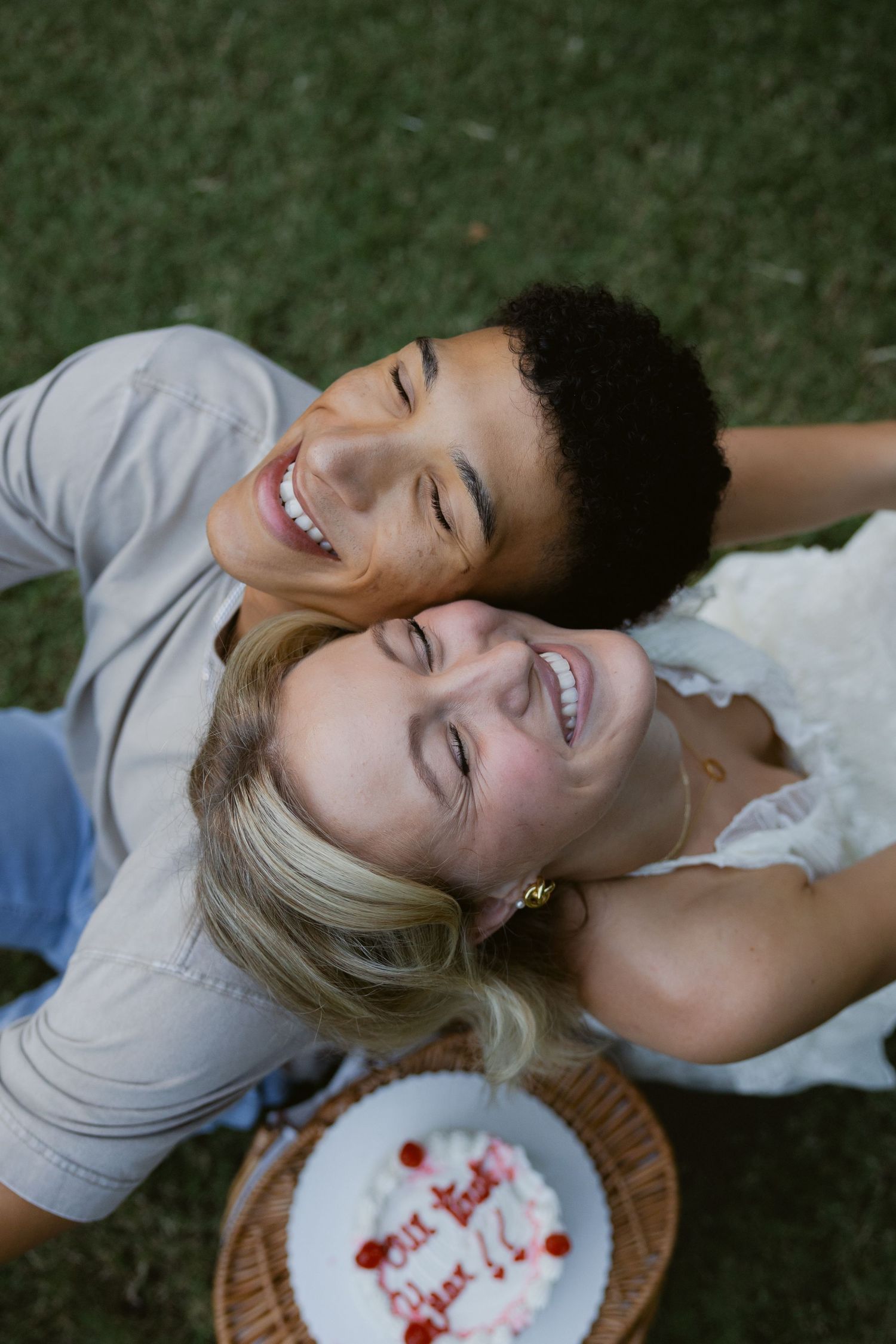A couple lying on a picnic blanket share laughter and joy while enjoying time together outdoors.