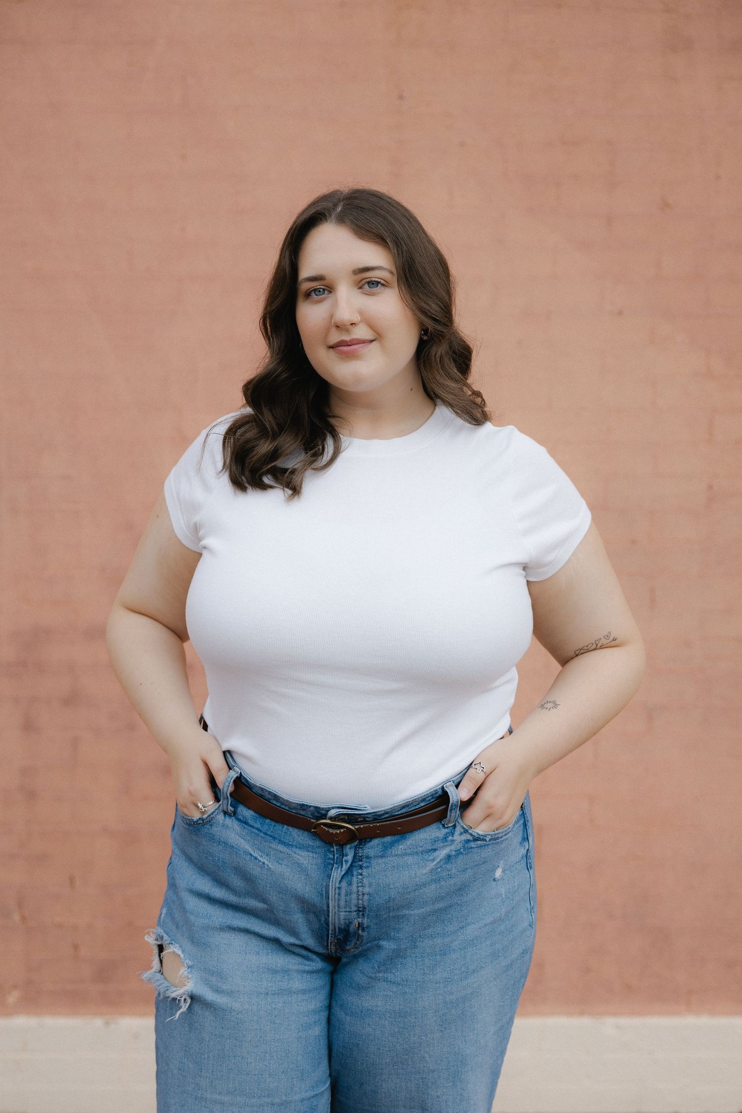A woman wearing a classic white t-shirt and blue jeans poses against a peachy-colored wall in a casual style shoot.