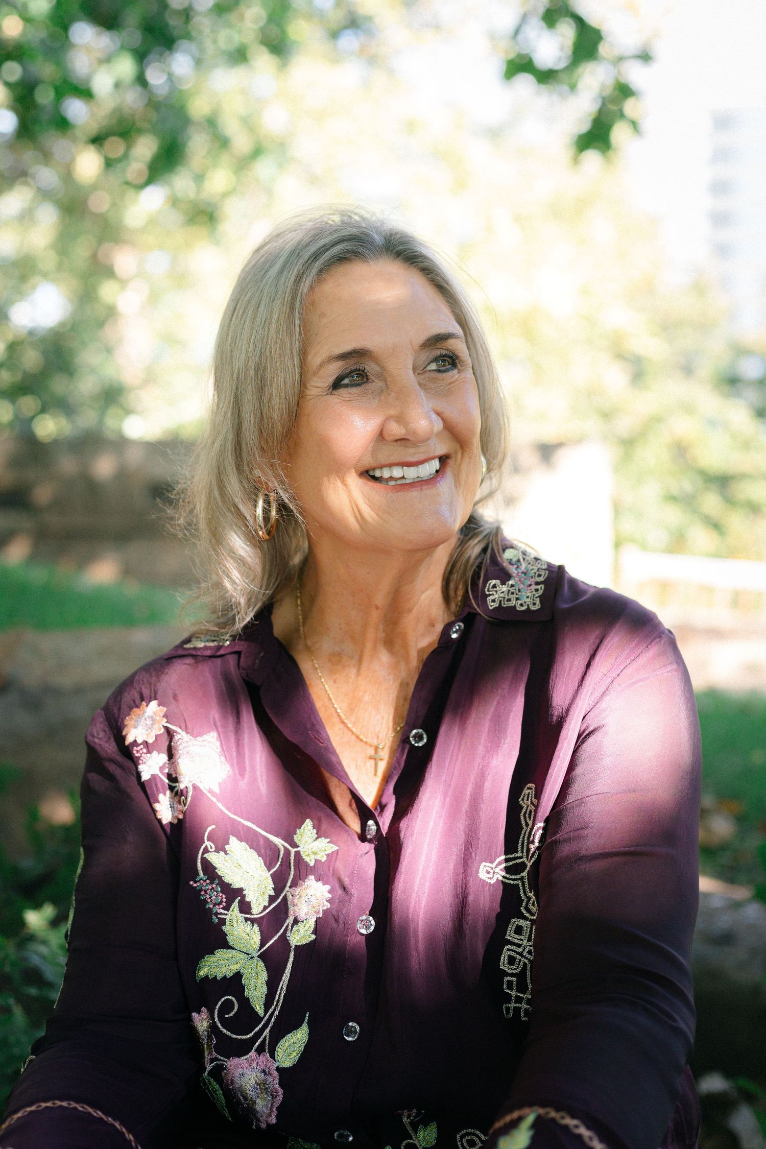 Portrait in garden setting wearing purple floral embroidered jacket.