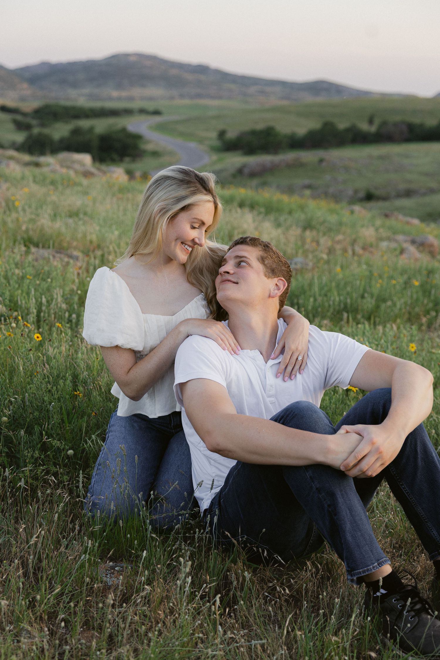 A couple sitting together in a grassy field at sunset, sharing intimate moments and laughter in nature.