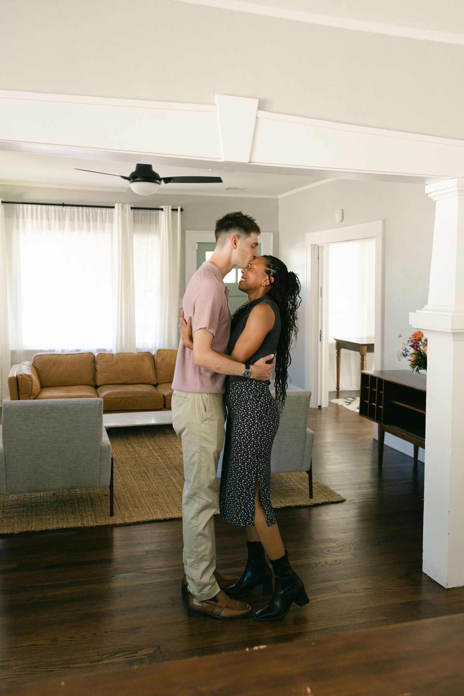 Interracial couple sharing a romantic kiss while embracing in a bright modern living room.