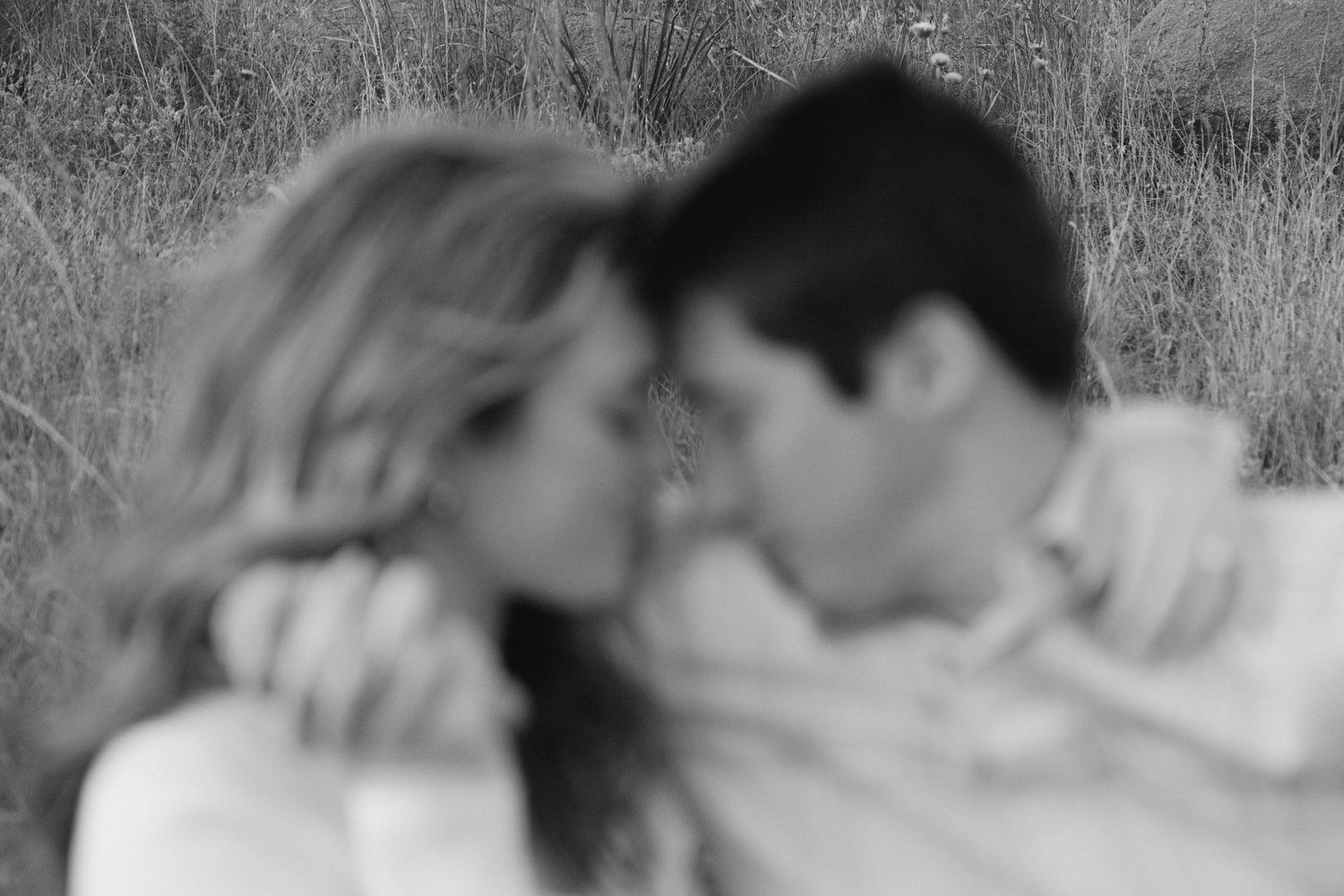 Black and white romantic photo of a couple in an intimate moment together in a grassy outdoor setting.