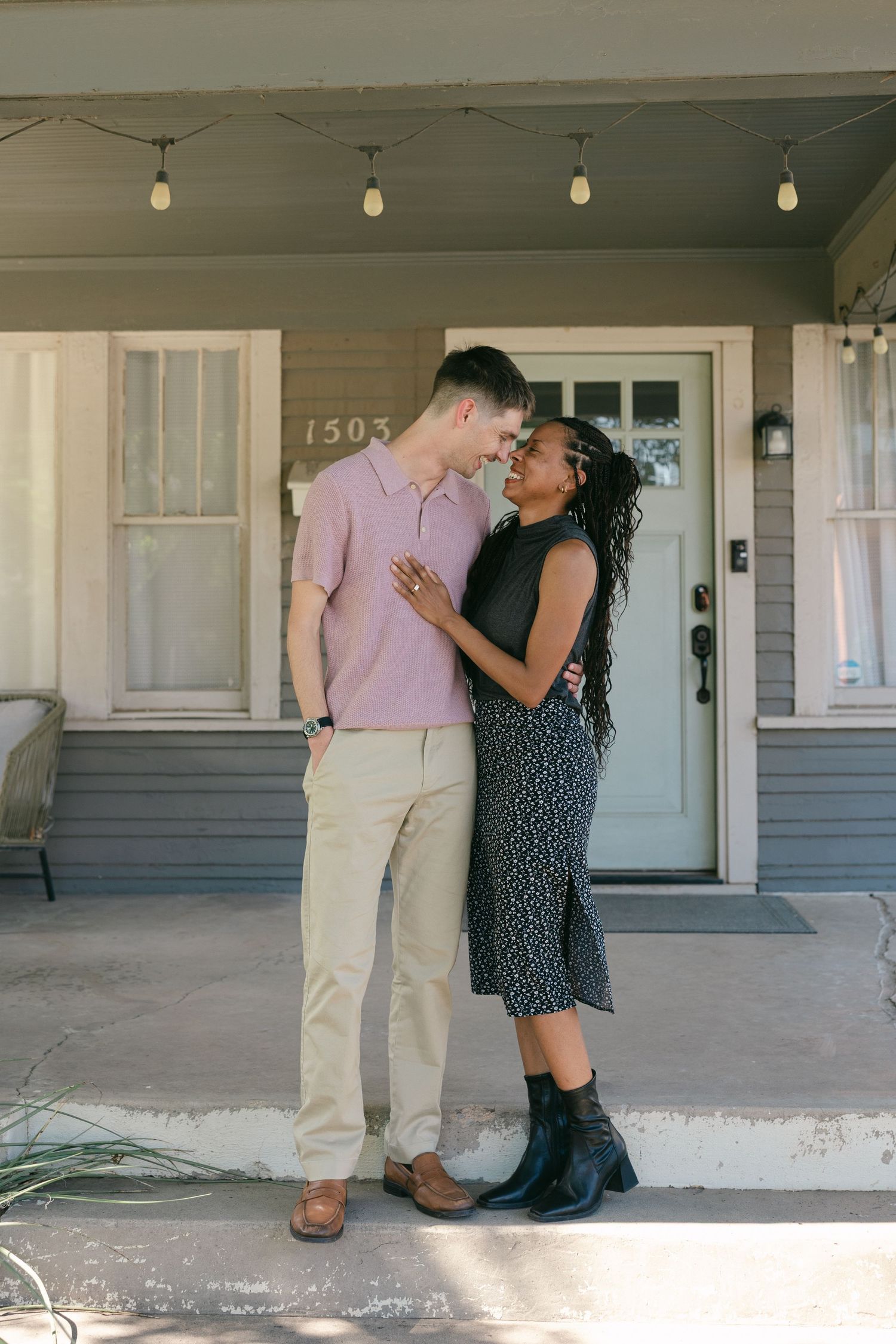 Romantic interracial couple nearly kissing while standing close together on a residential front porch.