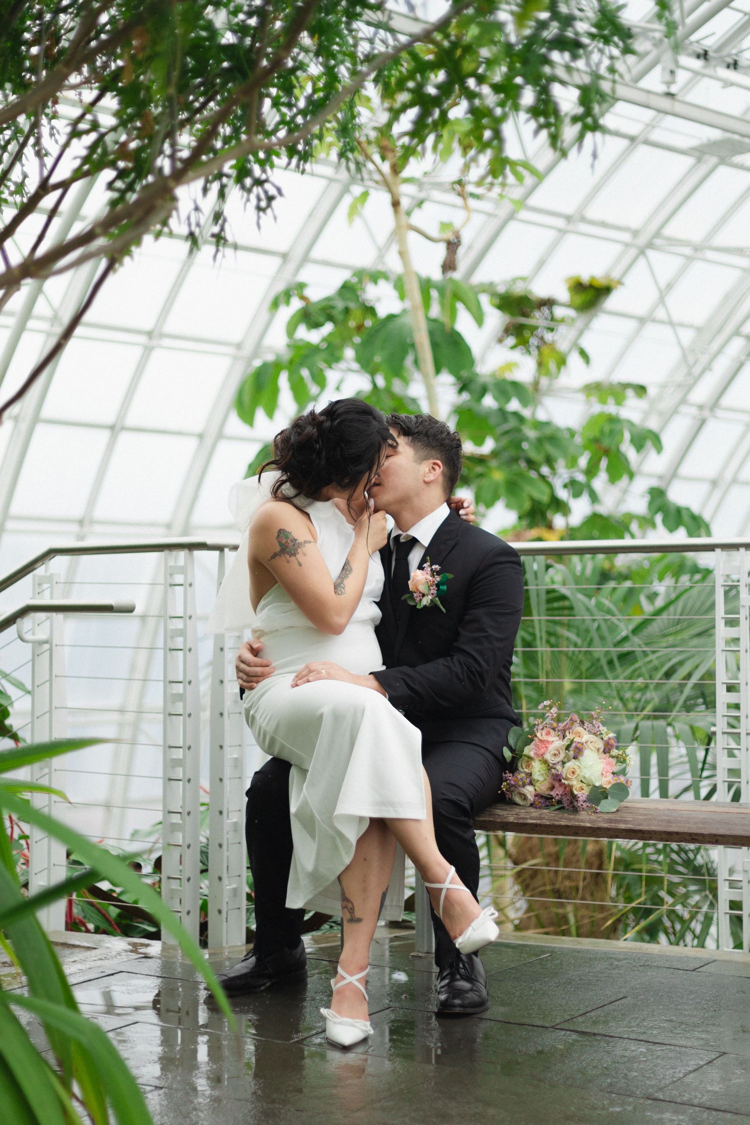 Romantic wedding couple embracing in a conservatory with lush greenery and natural light.