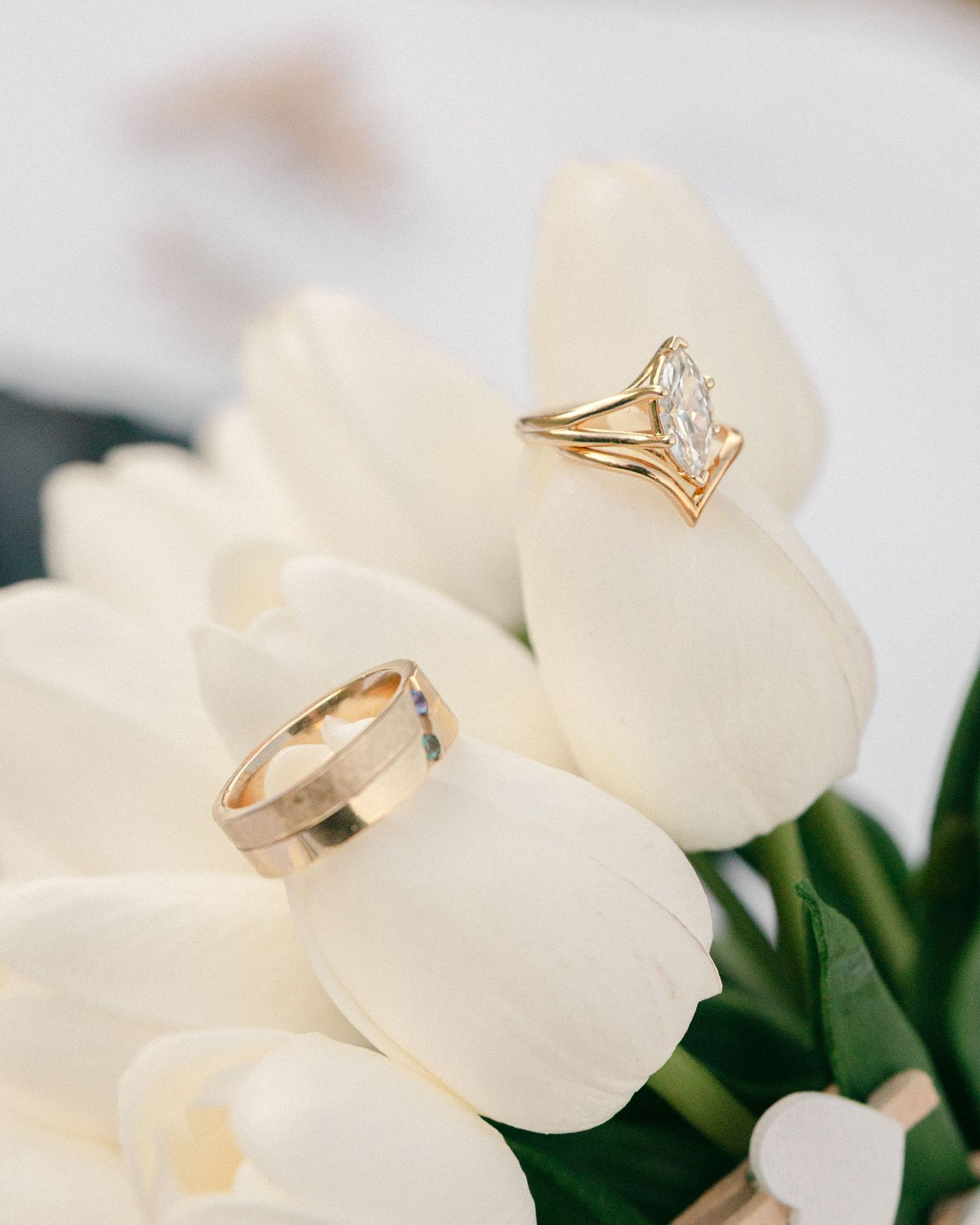 Gold wedding band and marquise diamond engagement ring resting on white tulip flowers.