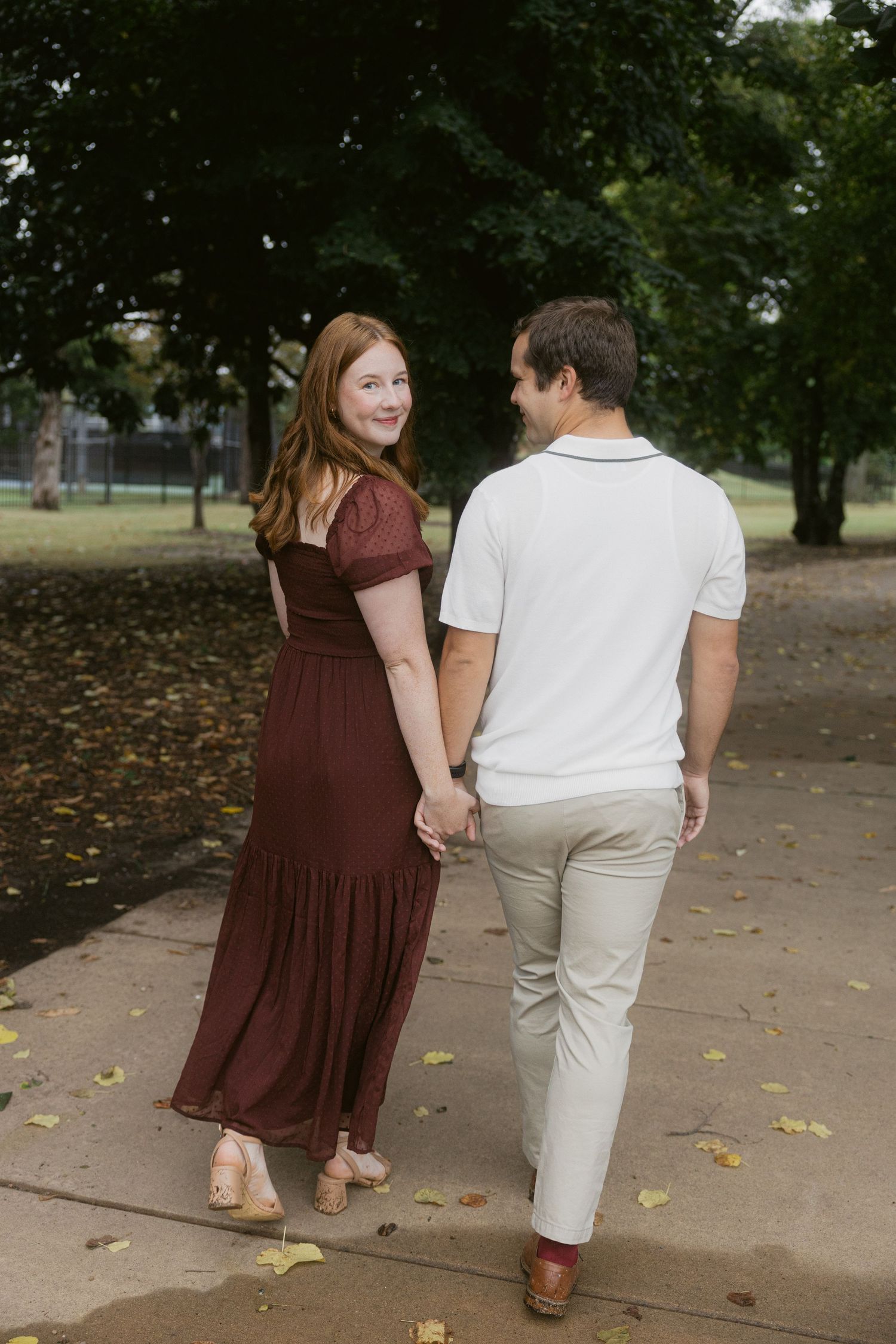 A couple walking hand in hand on an autumn path, dressed in burgundy and white outfits.