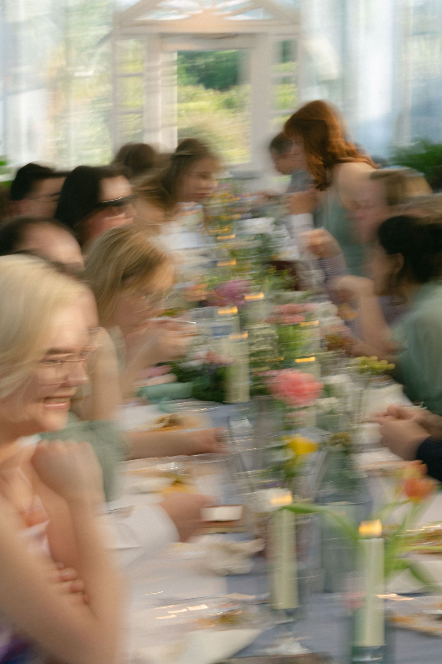 Blurred motion photo of elegantly dressed guests dining at a long flower-adorned table during a wedding reception.