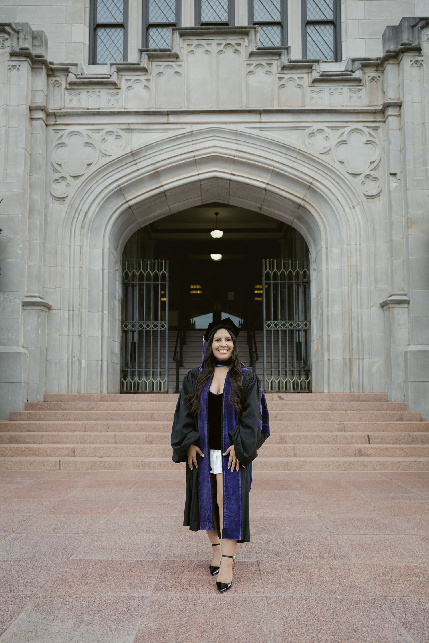 Graduation photos taken on stone steps of Gothic university building with decorative arched entrances.