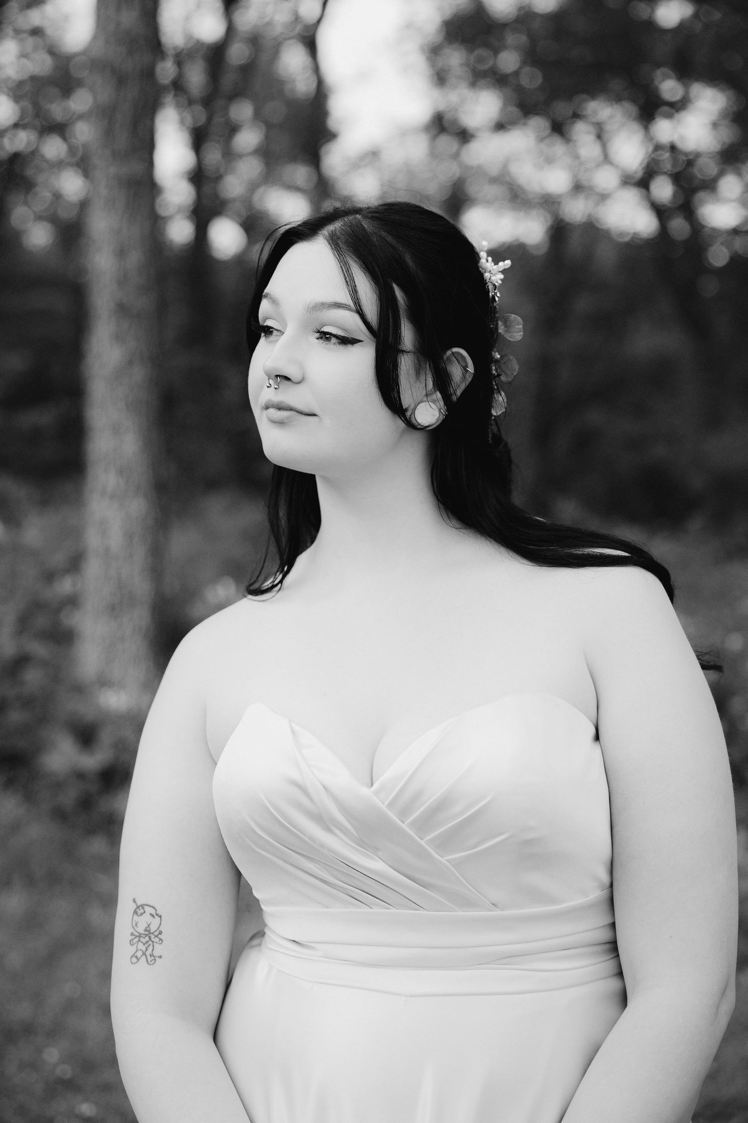 A bride in a strapless white wedding gown poses for a black and white portrait outdoors.