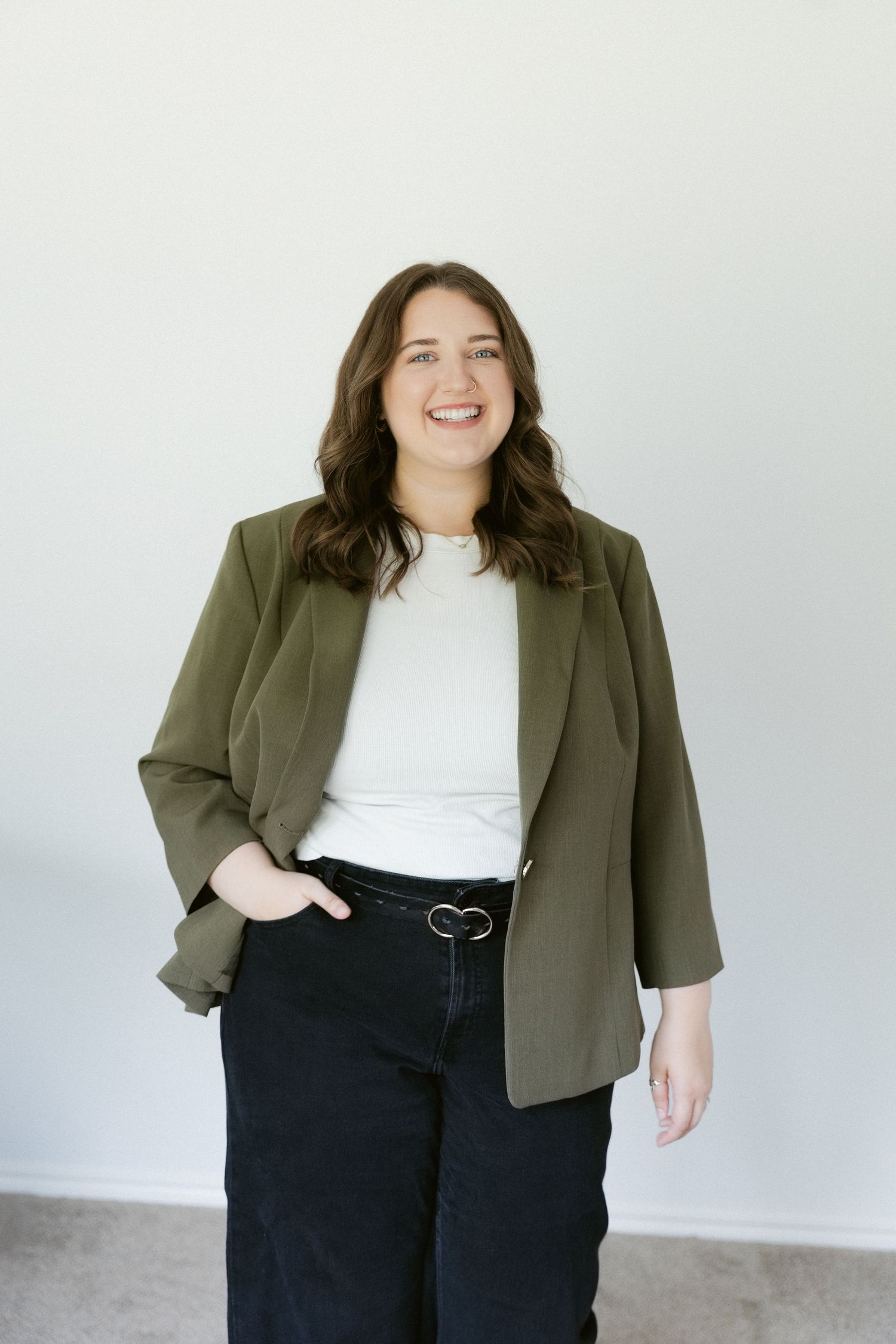 A person in a white top and olive blazer poses in a series of professional photos against a light background.