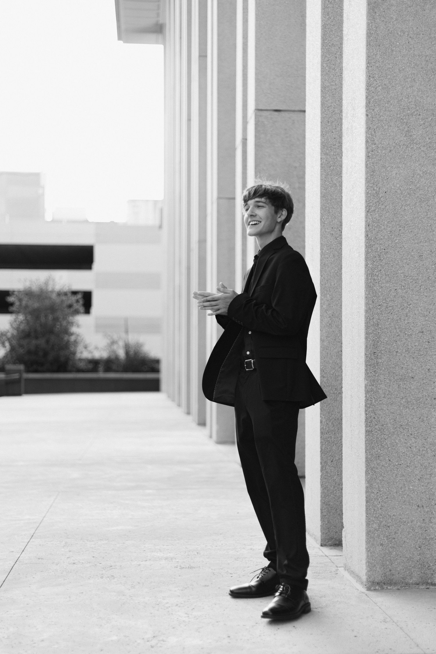 A figure in black attire stands between white architectural columns in a minimalist setting creating a striking contrast.