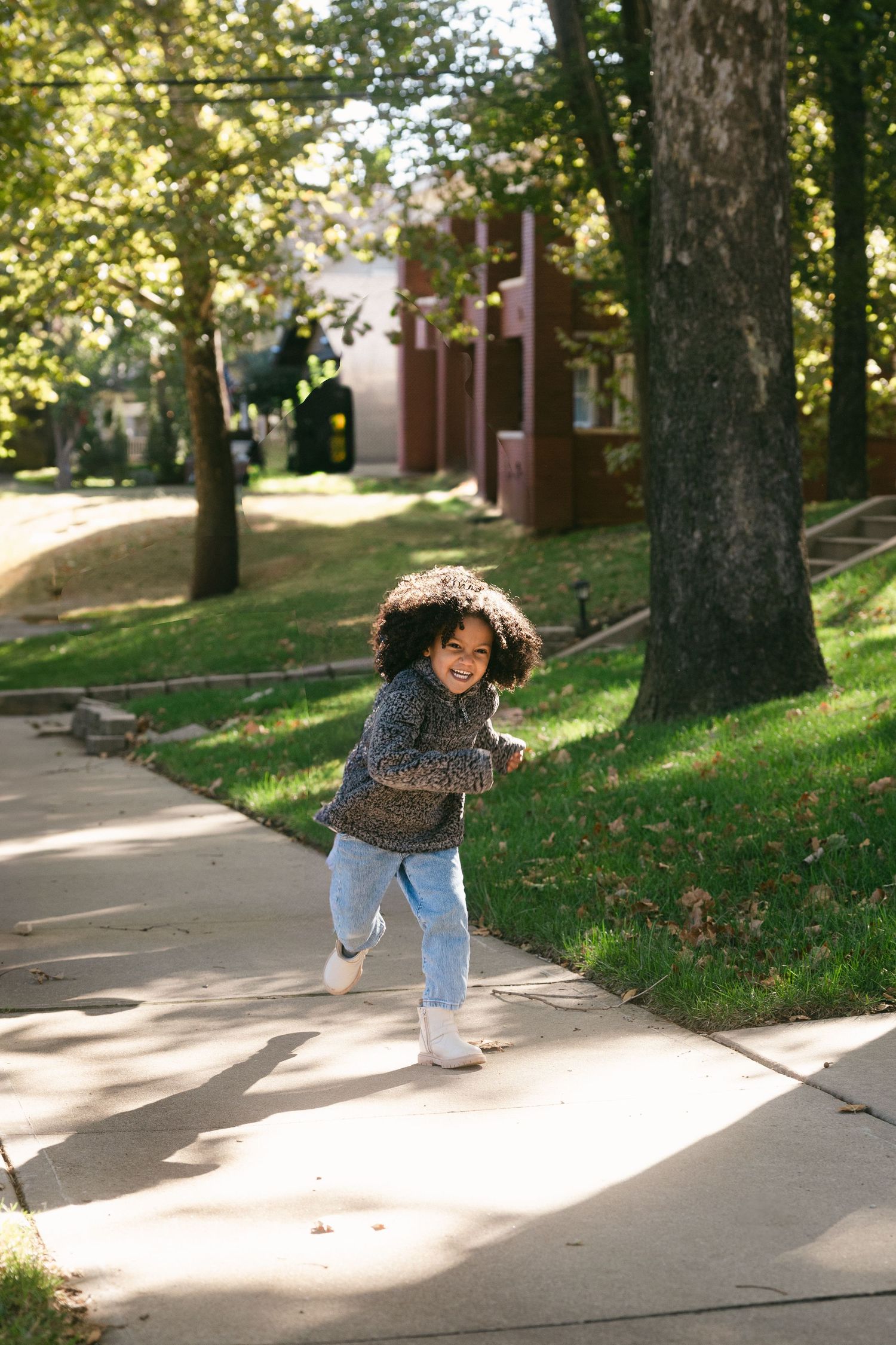 A person walks down a sunlit sidewalk on a fall day casting long shadows among trees and fallen leaves.