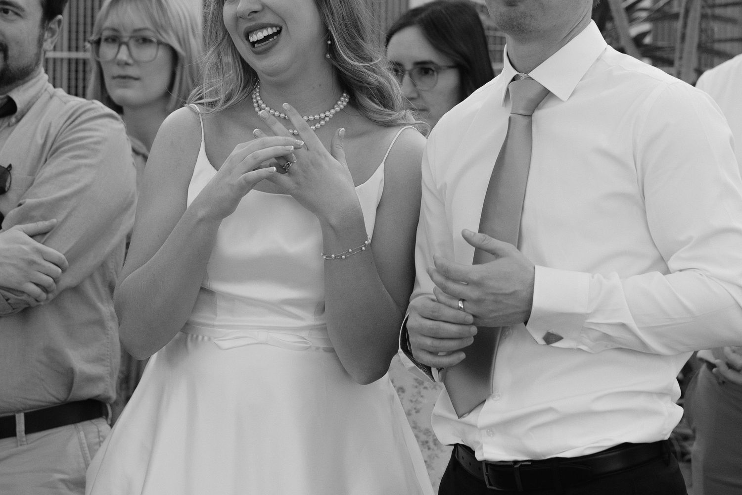 Black and white photo of a laughing bride in white dress and groom in tie at a wedding reception.