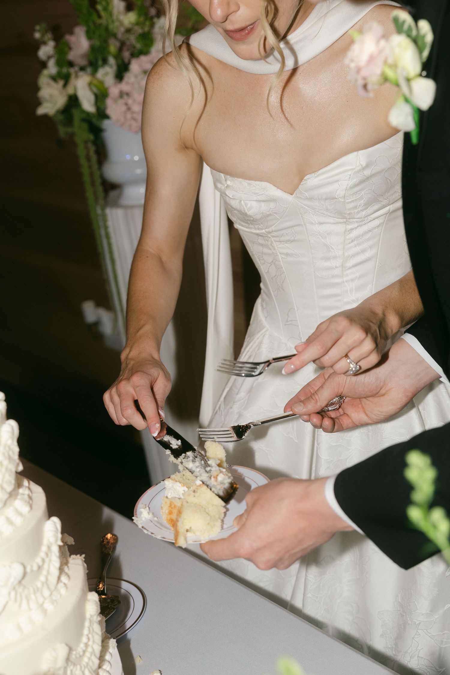 Bride in strapless white gown and groom cut their tiered white wedding cake together at their reception.
