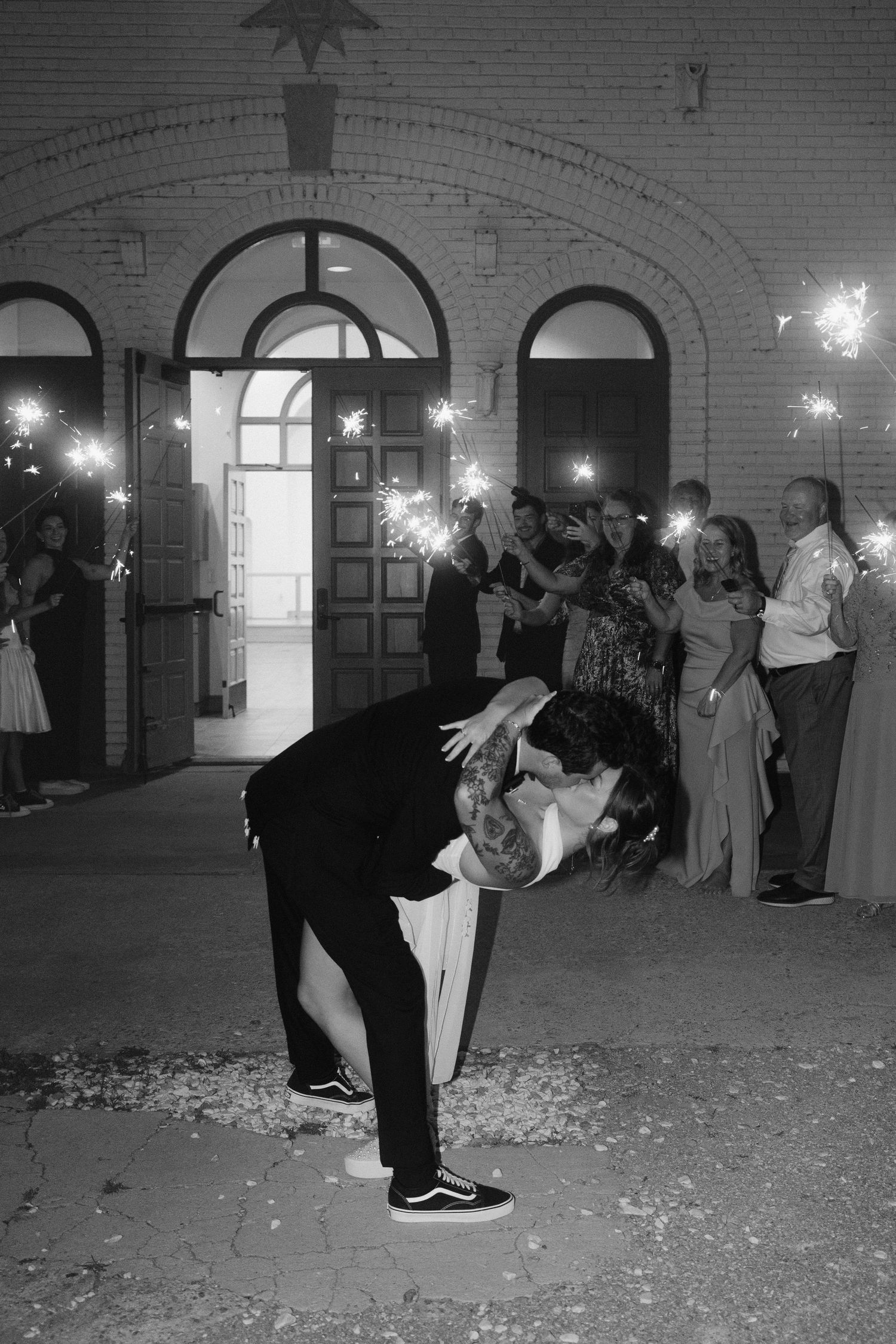 Black and white photo of groom dipping bride during sparkler send-off exit at wedding reception.