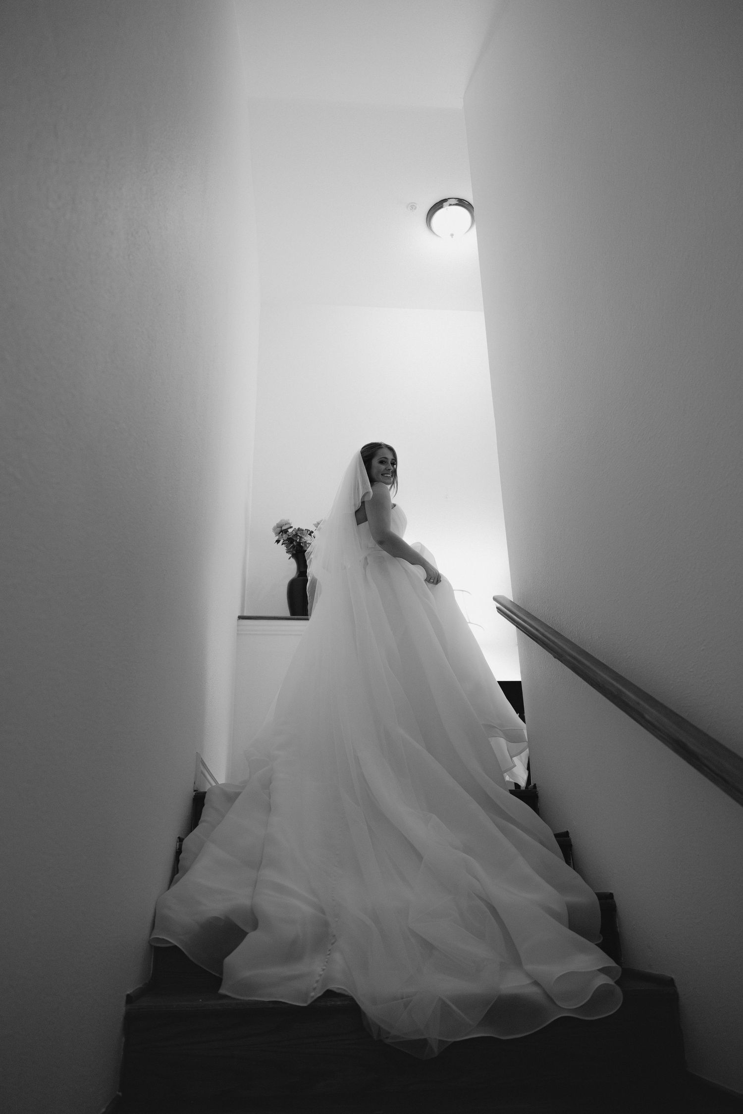 A dramatic black and white photo of a bride in a flowing gown descending a staircase.