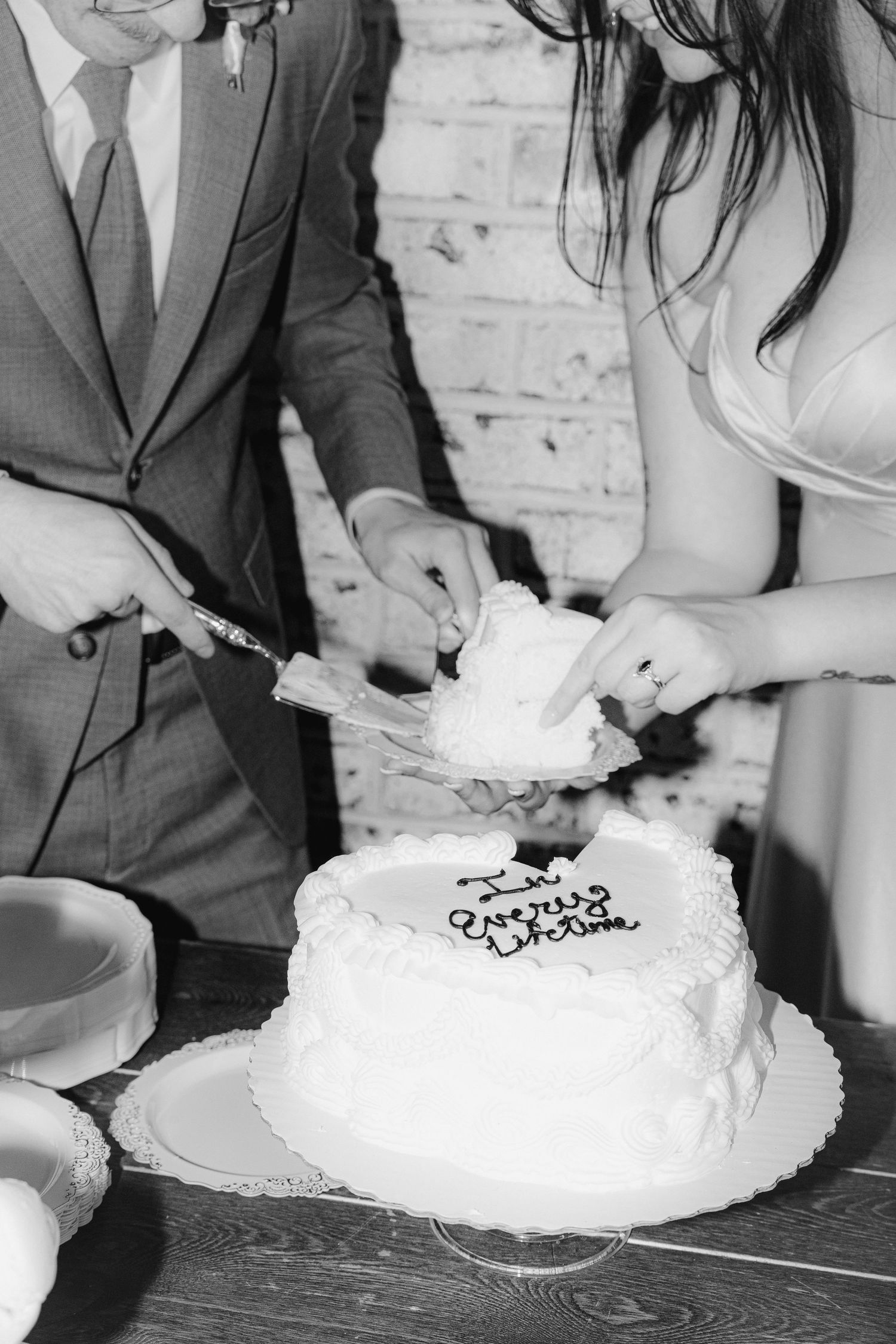 Newlyweds cut into their white wedding cake together during their reception celebration.