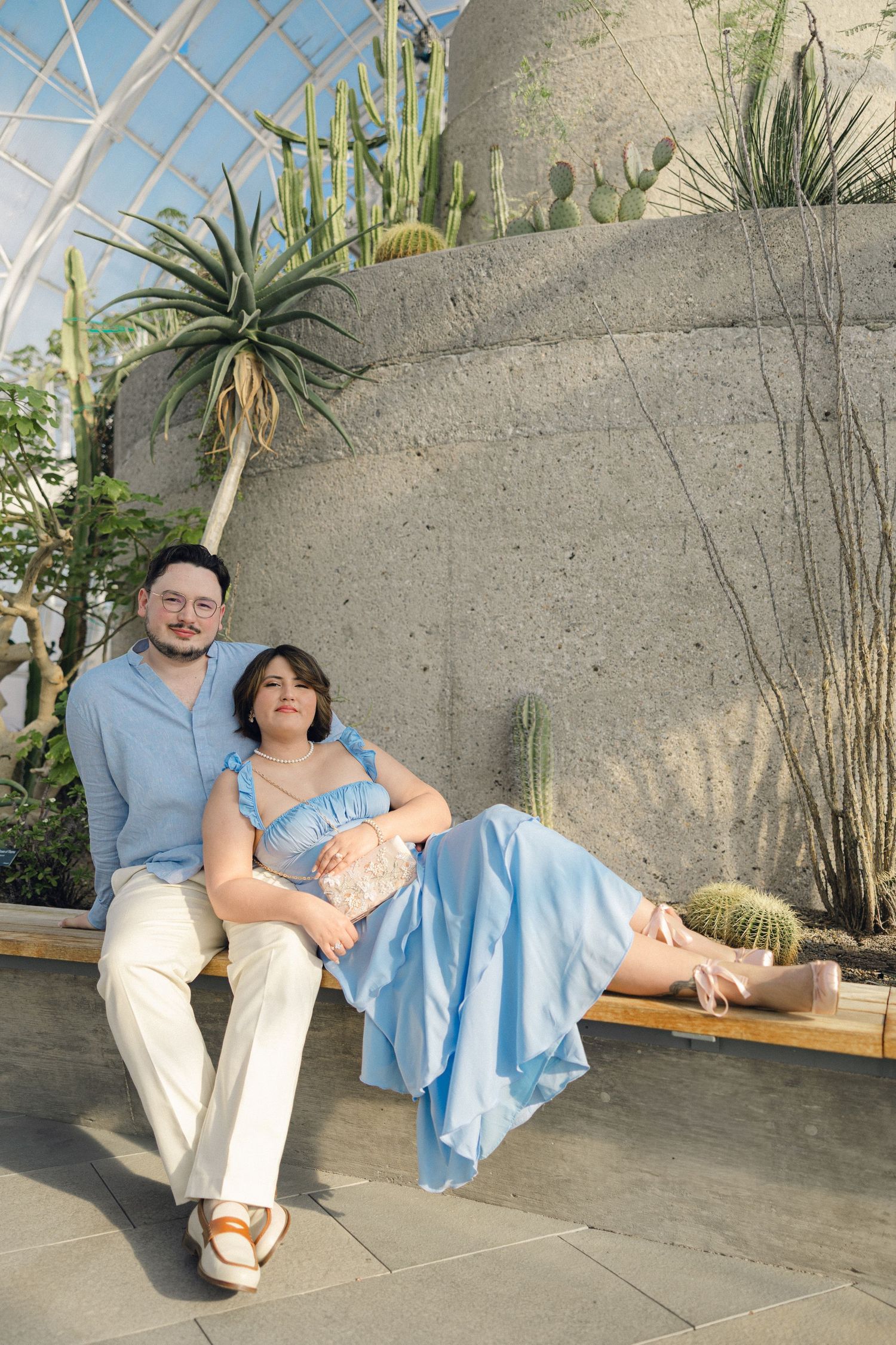 Couple sitting together on a bench in a botanical garden greenhouse with cacti and succulents.