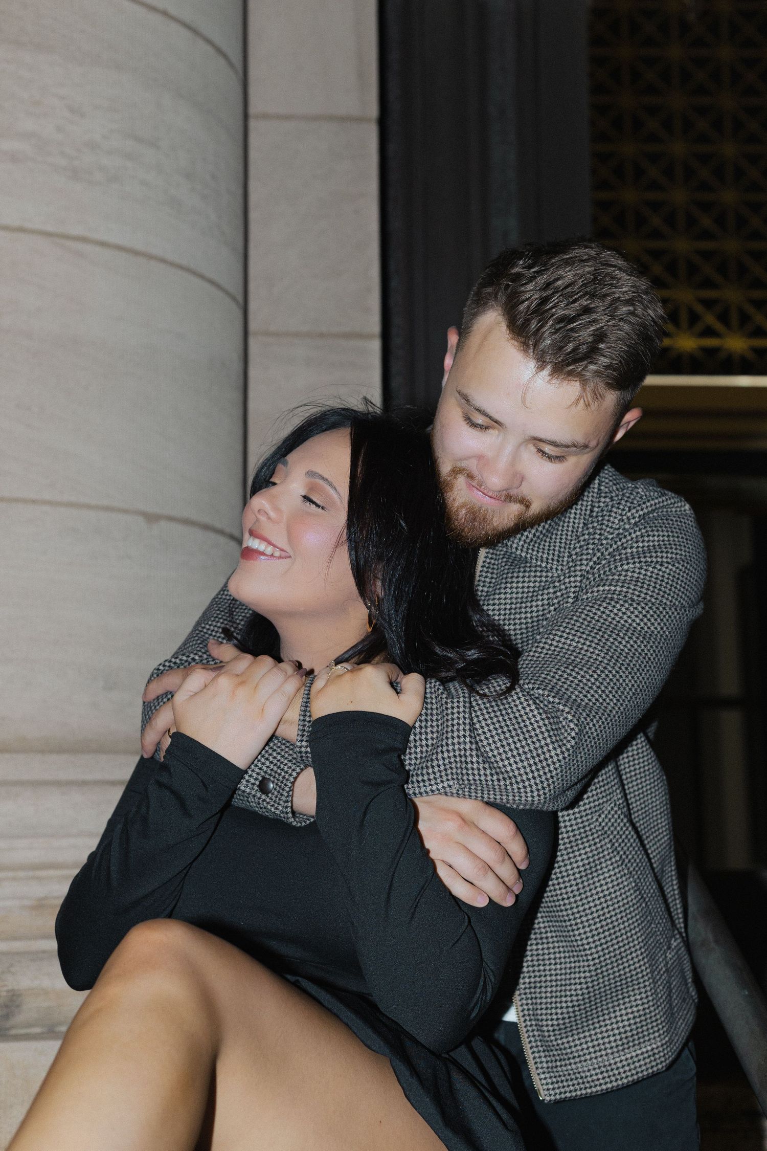 Romantic couple sharing an intimate moment against a stone column at night.