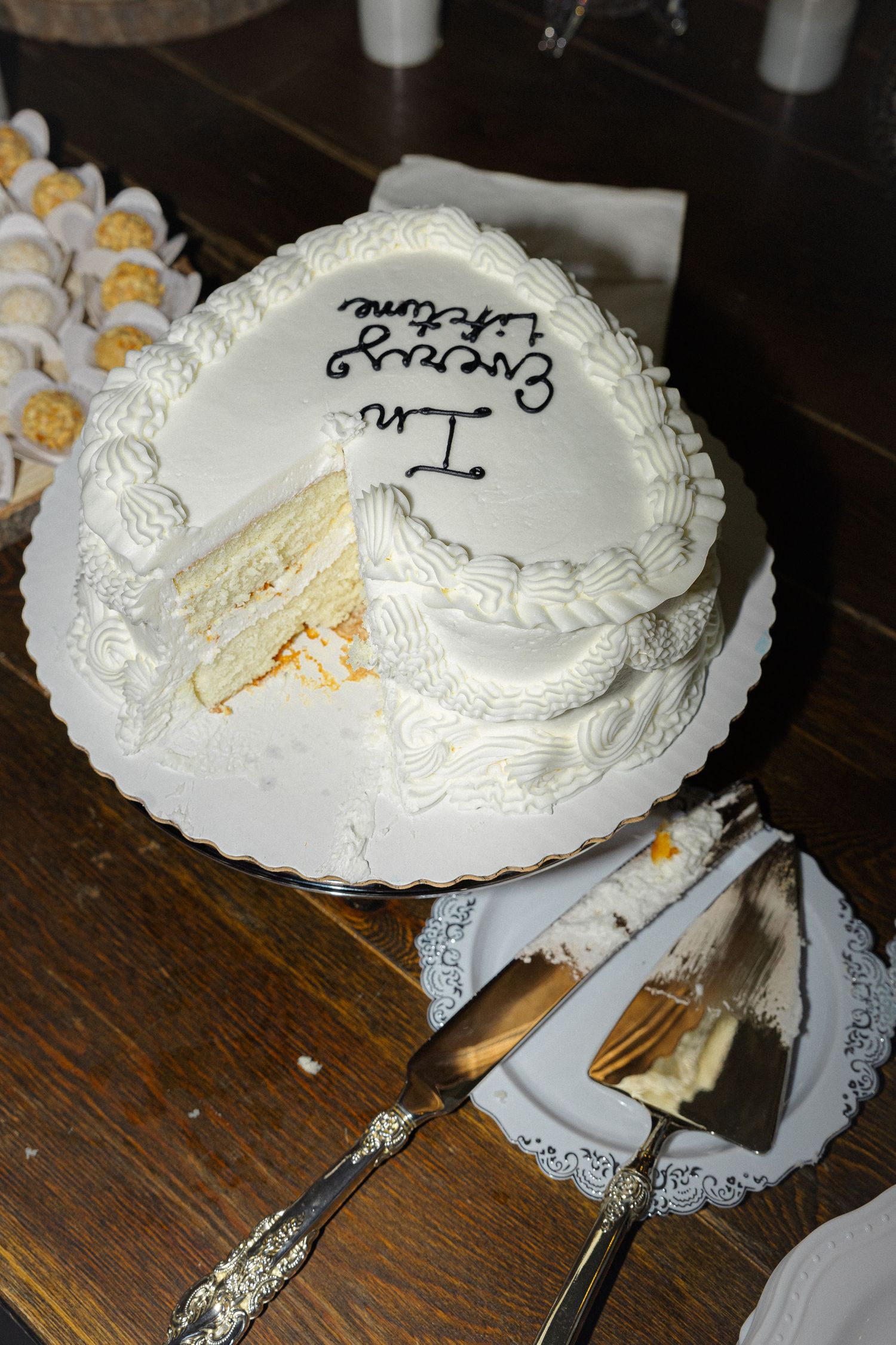 A white wedding cake with ornate frosting details and decorative serving utensils on a dark wooden table.