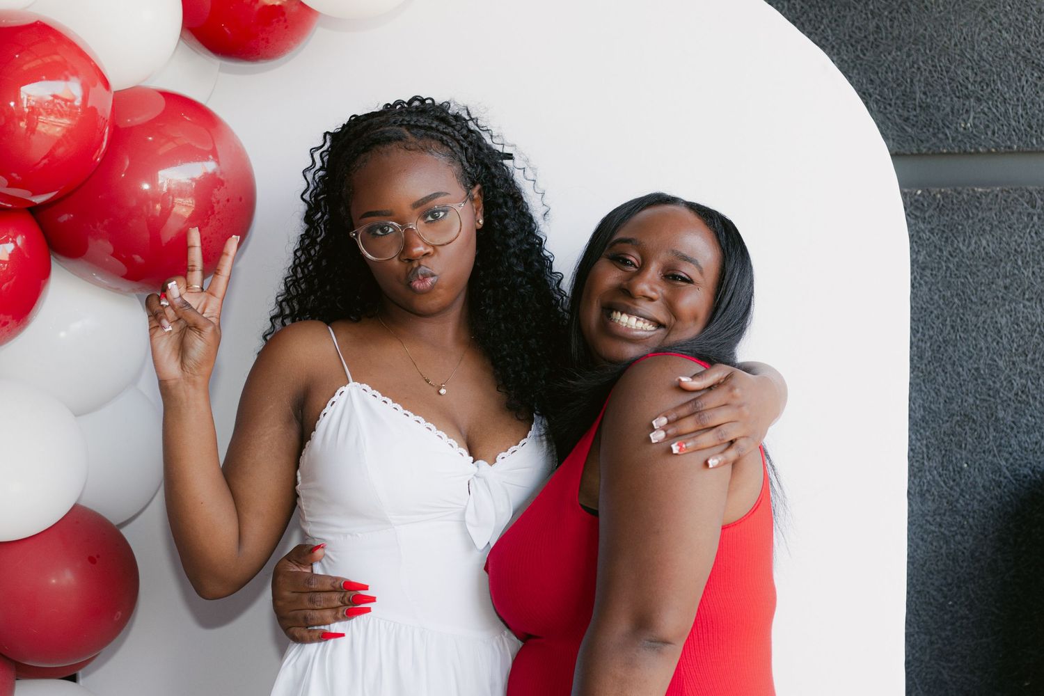 Joyful people pose together with red and white balloons against a grey wall during a photo session.