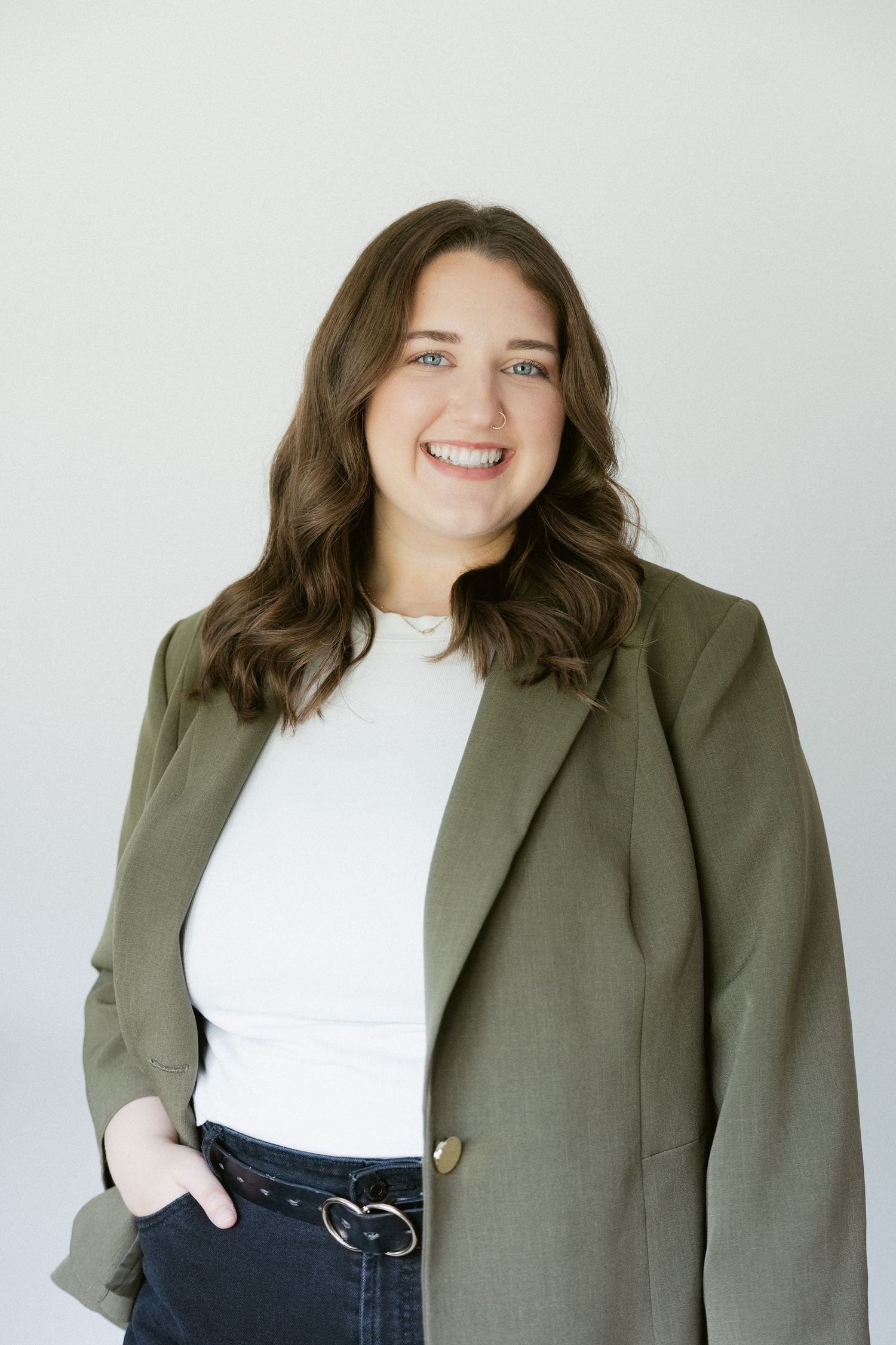 Business professional in olive blazer and white top smiles warmly against light background in photo series.