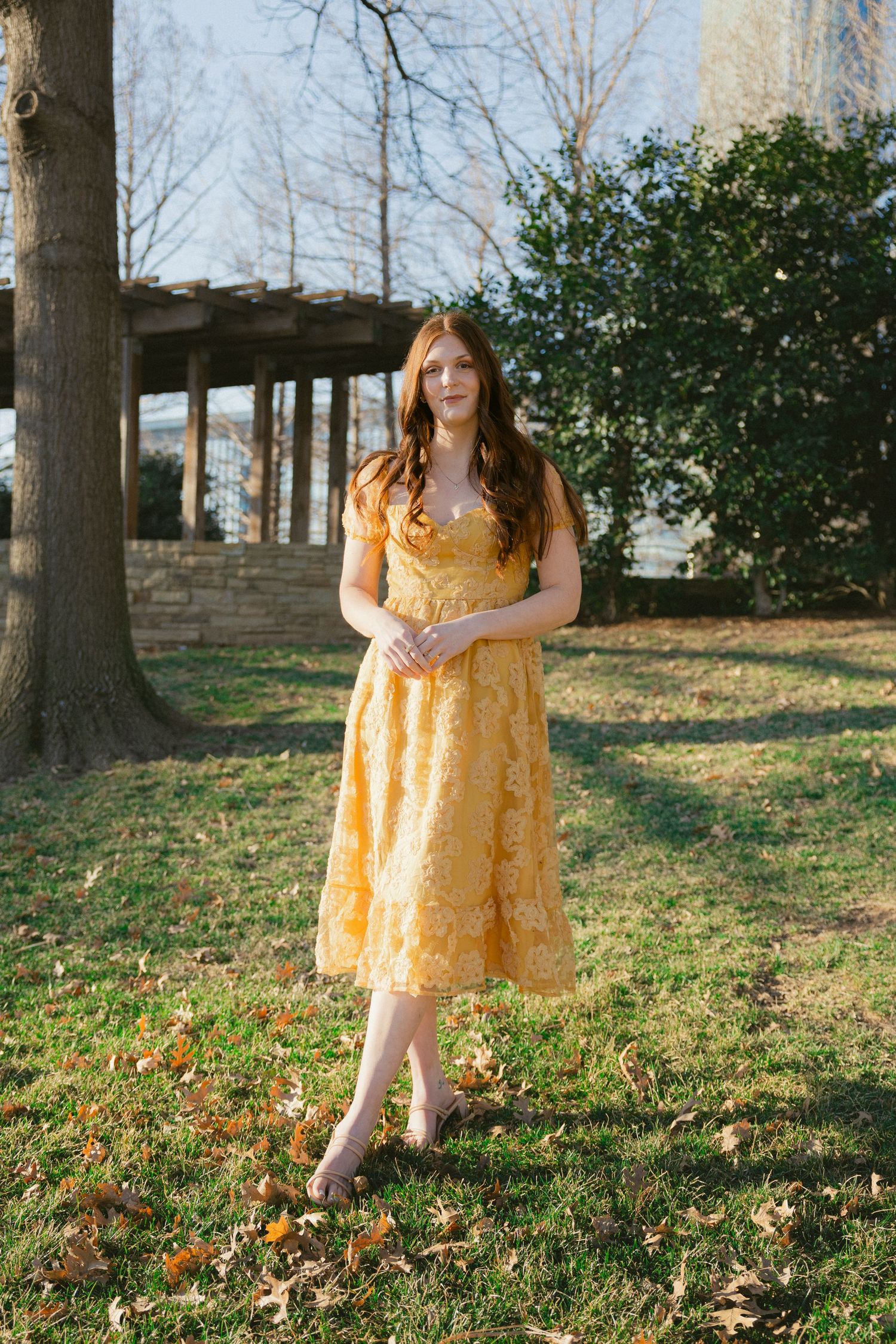 Someone in a yellow floral dress twirls playfully in a grassy park setting during autumn.